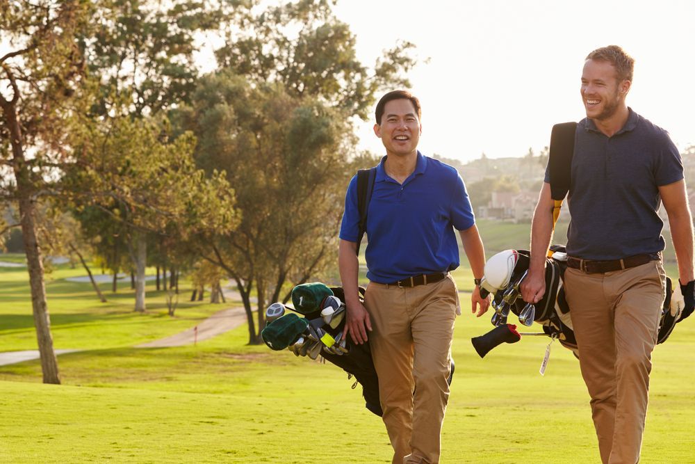 Two Male Golfers Walking Along Fairway Carrying Bags ©Monkey Business Images