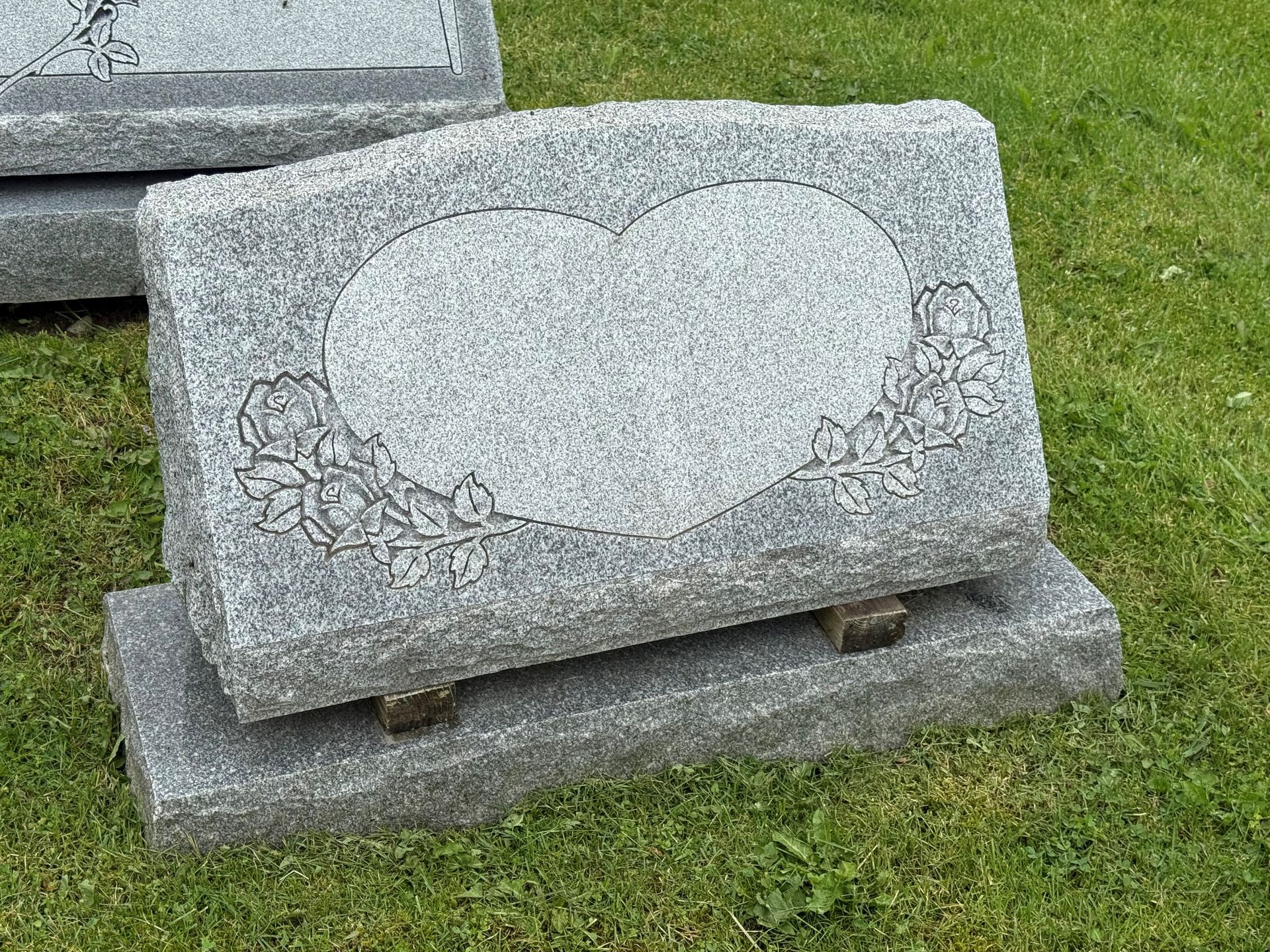 A gravestone with a heart carved into it is sitting in the grass.