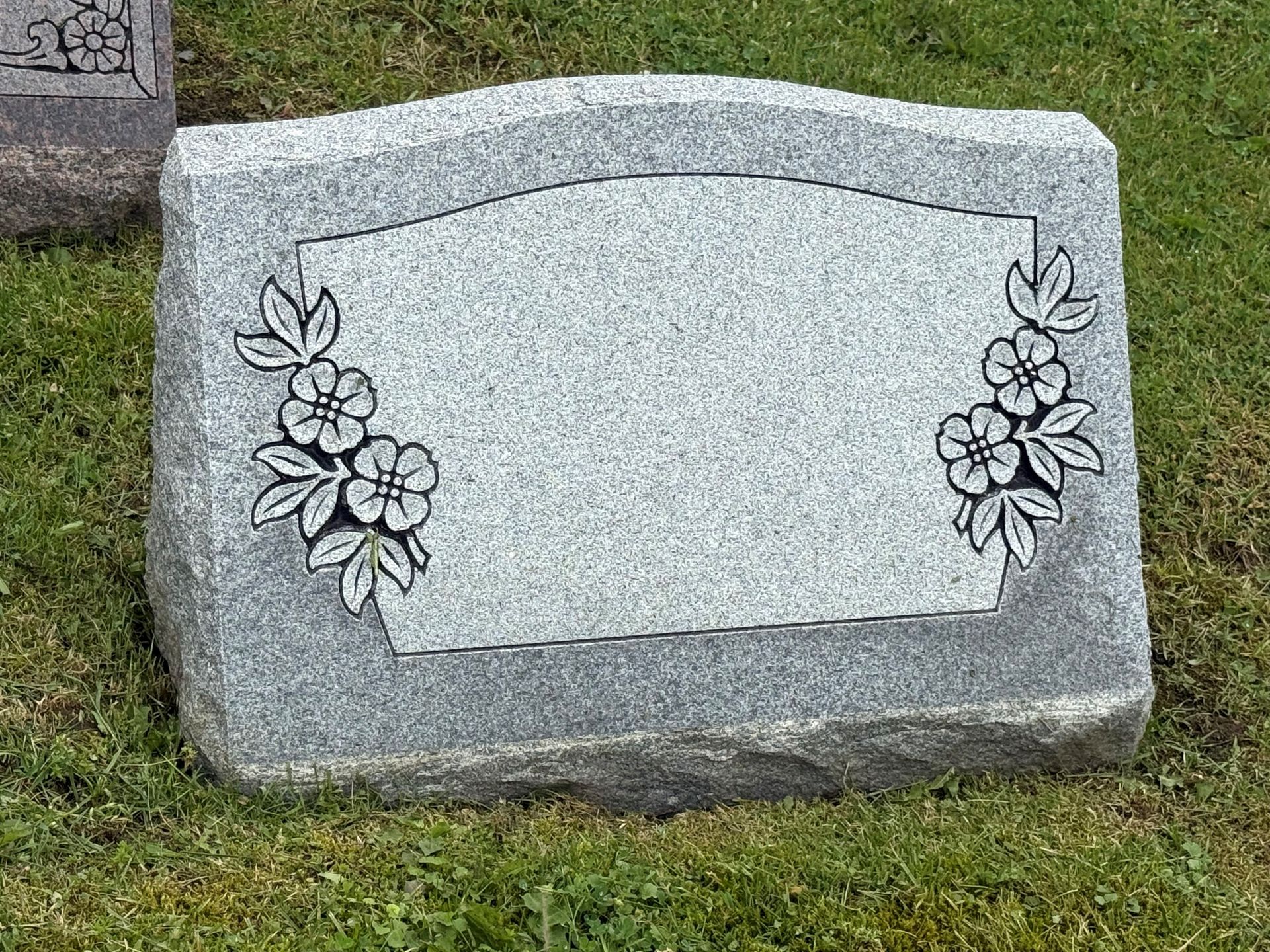 A gravestone with flowers carved into it is sitting in the grass.