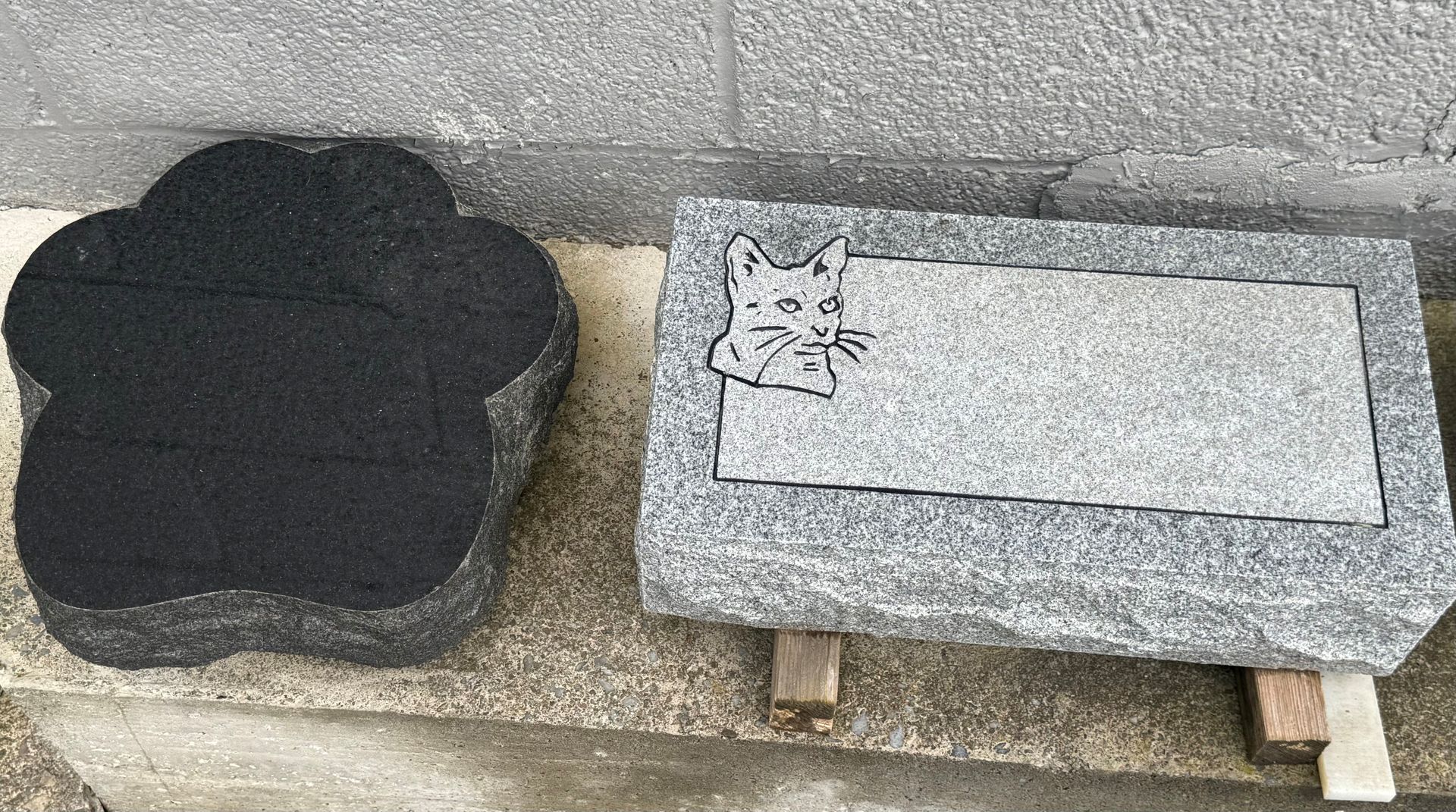 A gravestone with a cat on it is sitting next to a black stone.