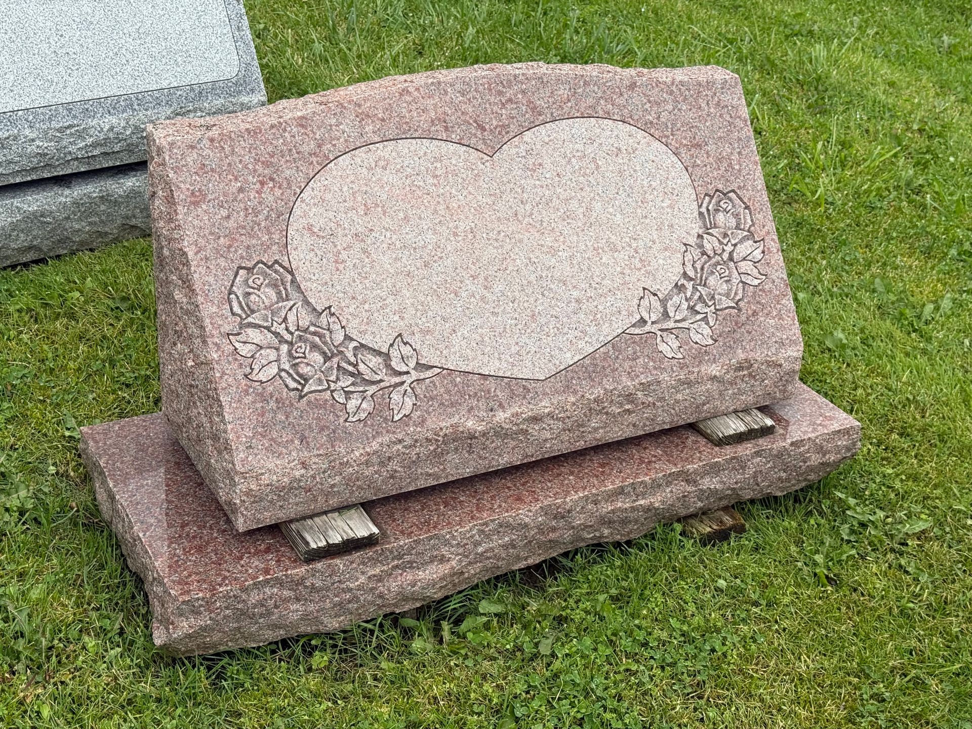 A gravestone with a heart on it is sitting in the grass.