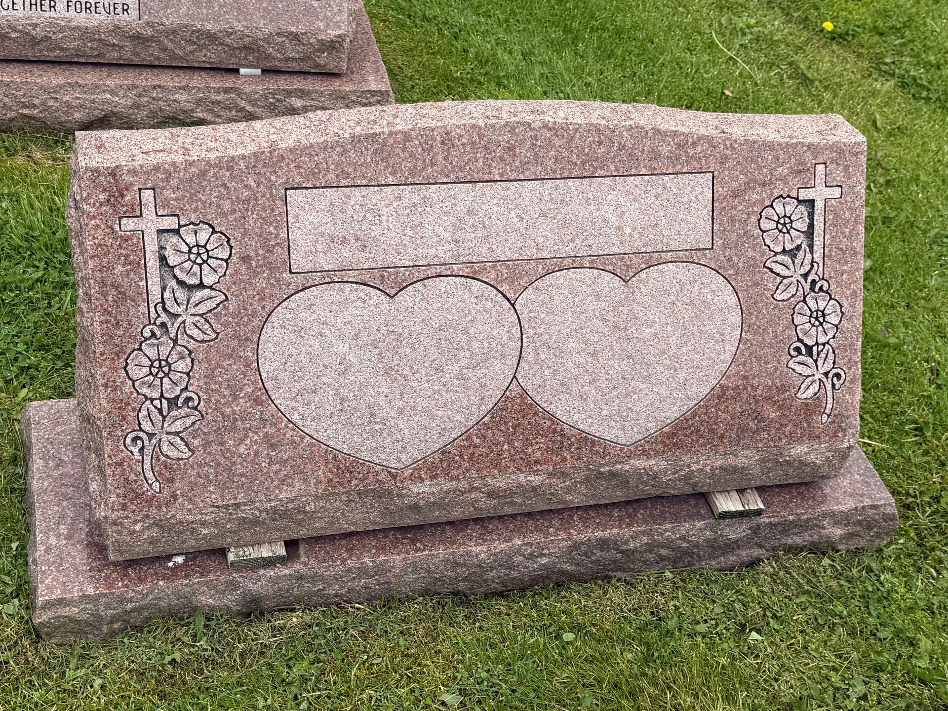 A gravestone with two hearts carved into it is sitting on top of a lush green field.