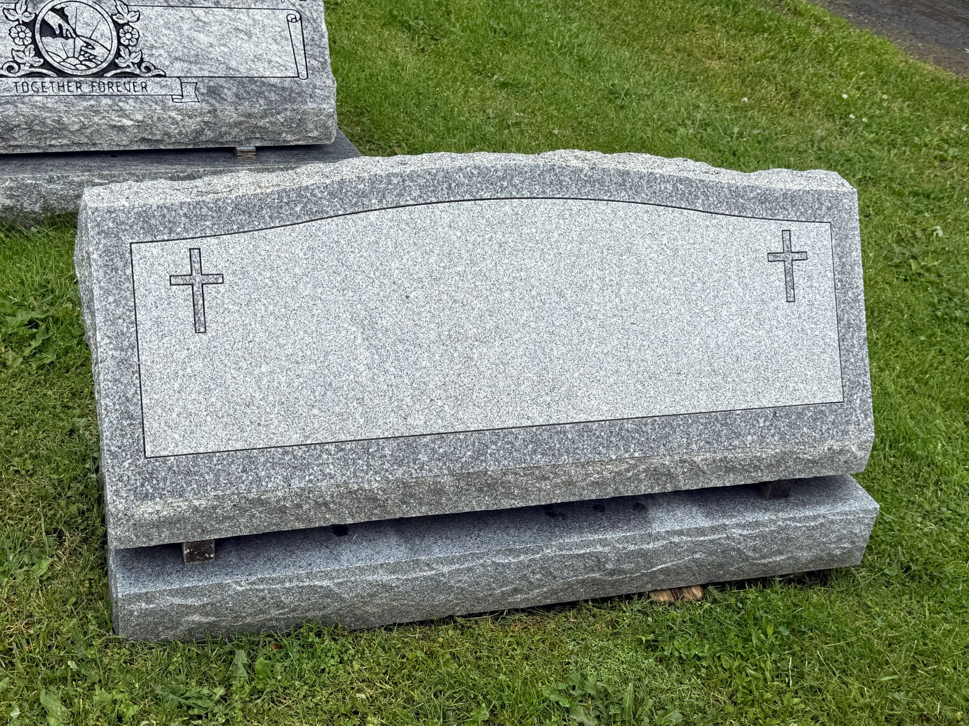 A gravestone with a cross on it is sitting in the grass.