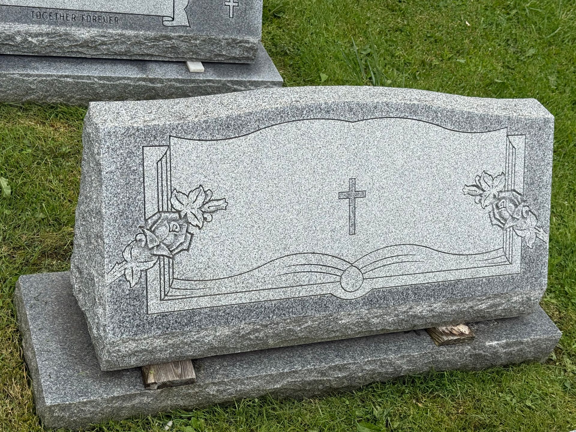 A gravestone with a cross on it is sitting in the grass.