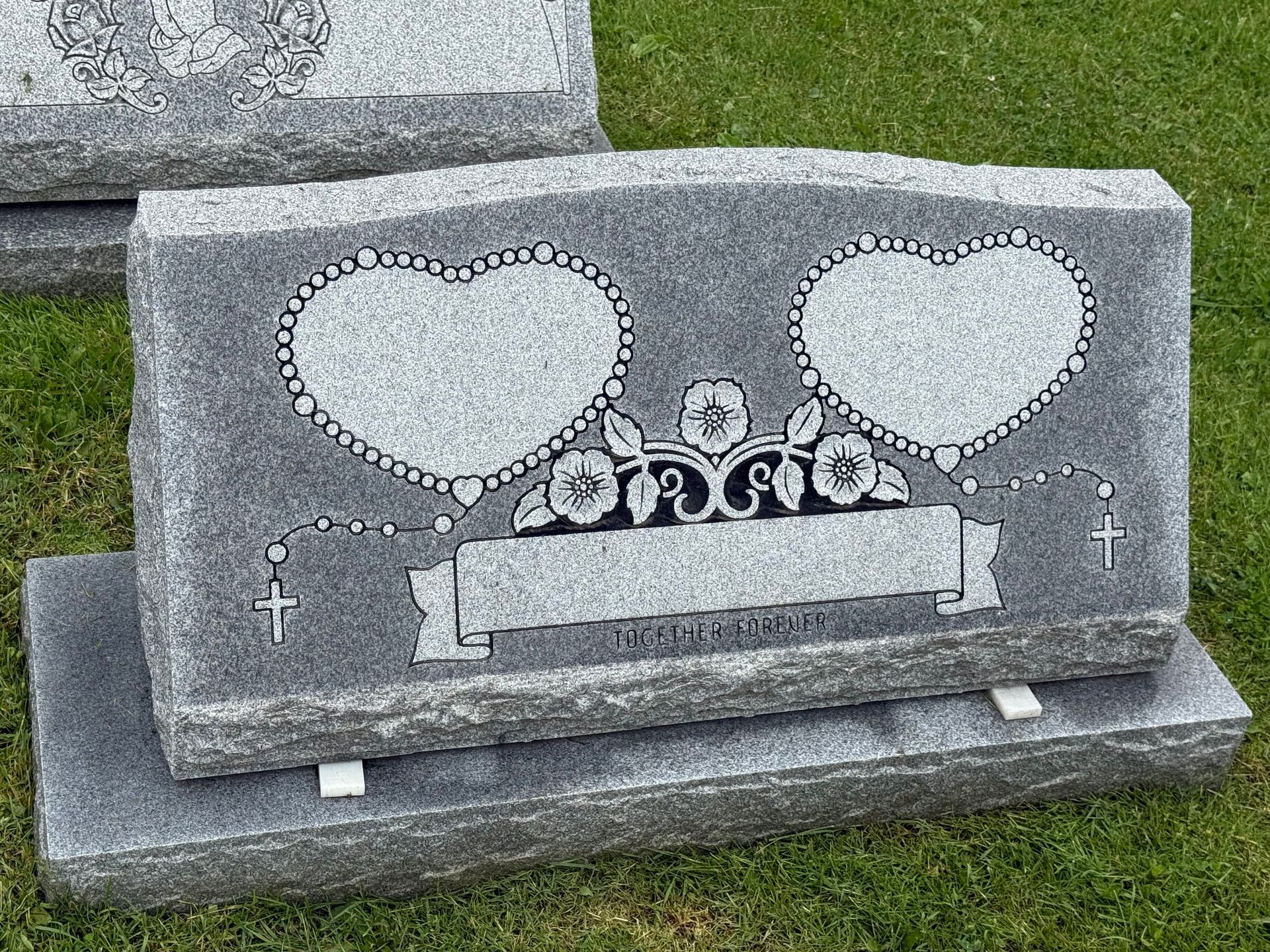 A gravestone with two hearts on it is sitting on top of a grass covered field.