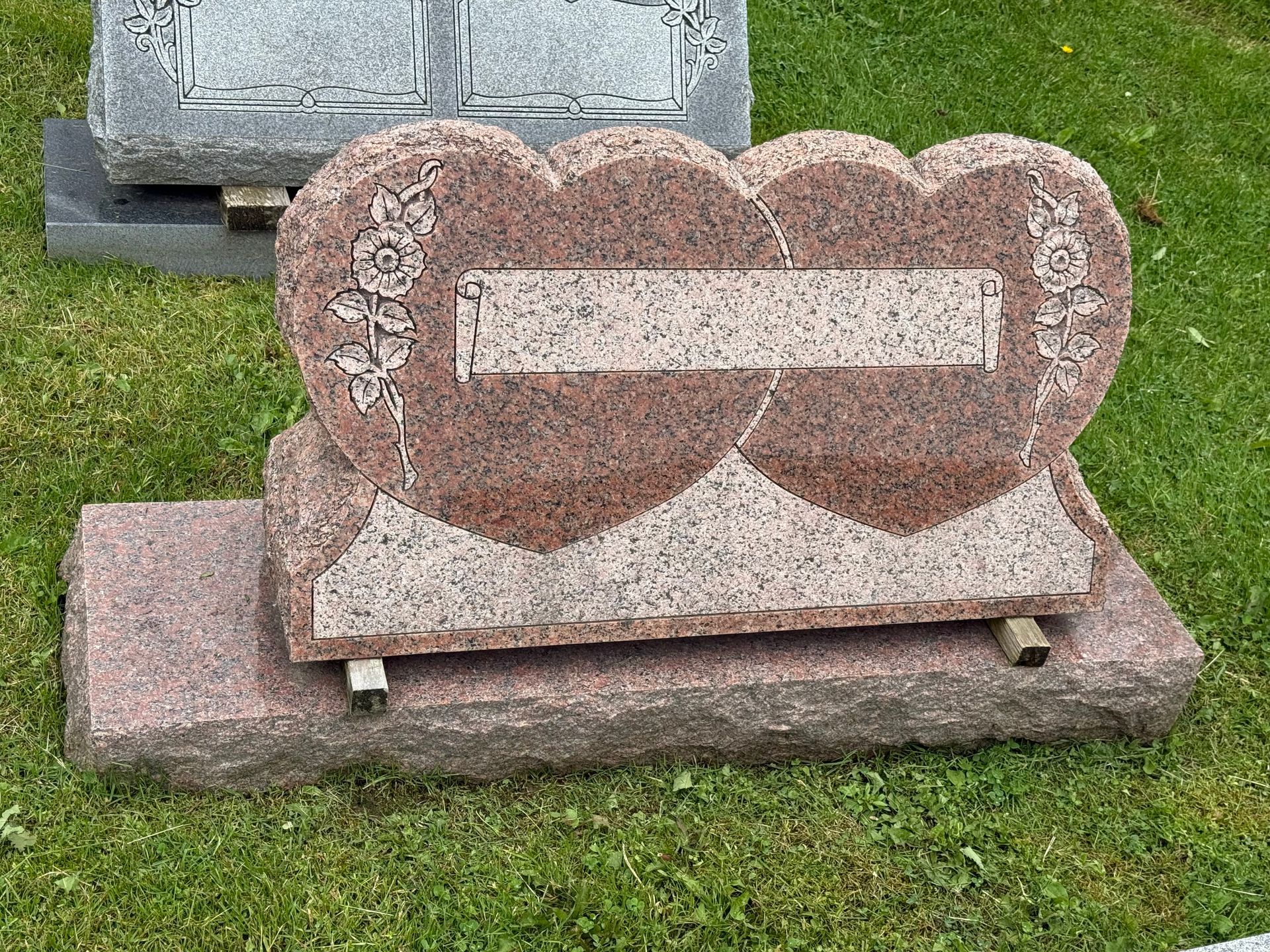 A gravestone in the shape of a heart is sitting in the grass.