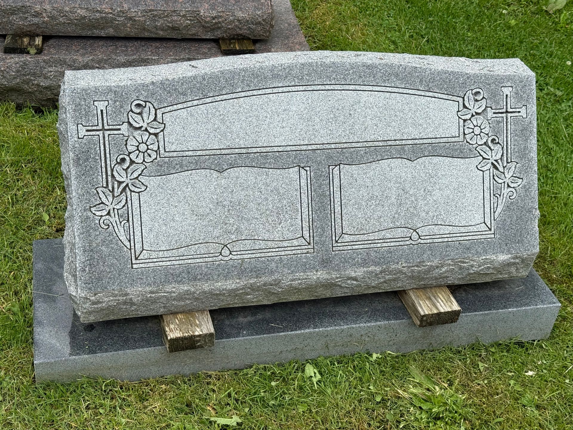 A gravestone is sitting on top of a wooden base in the grass.