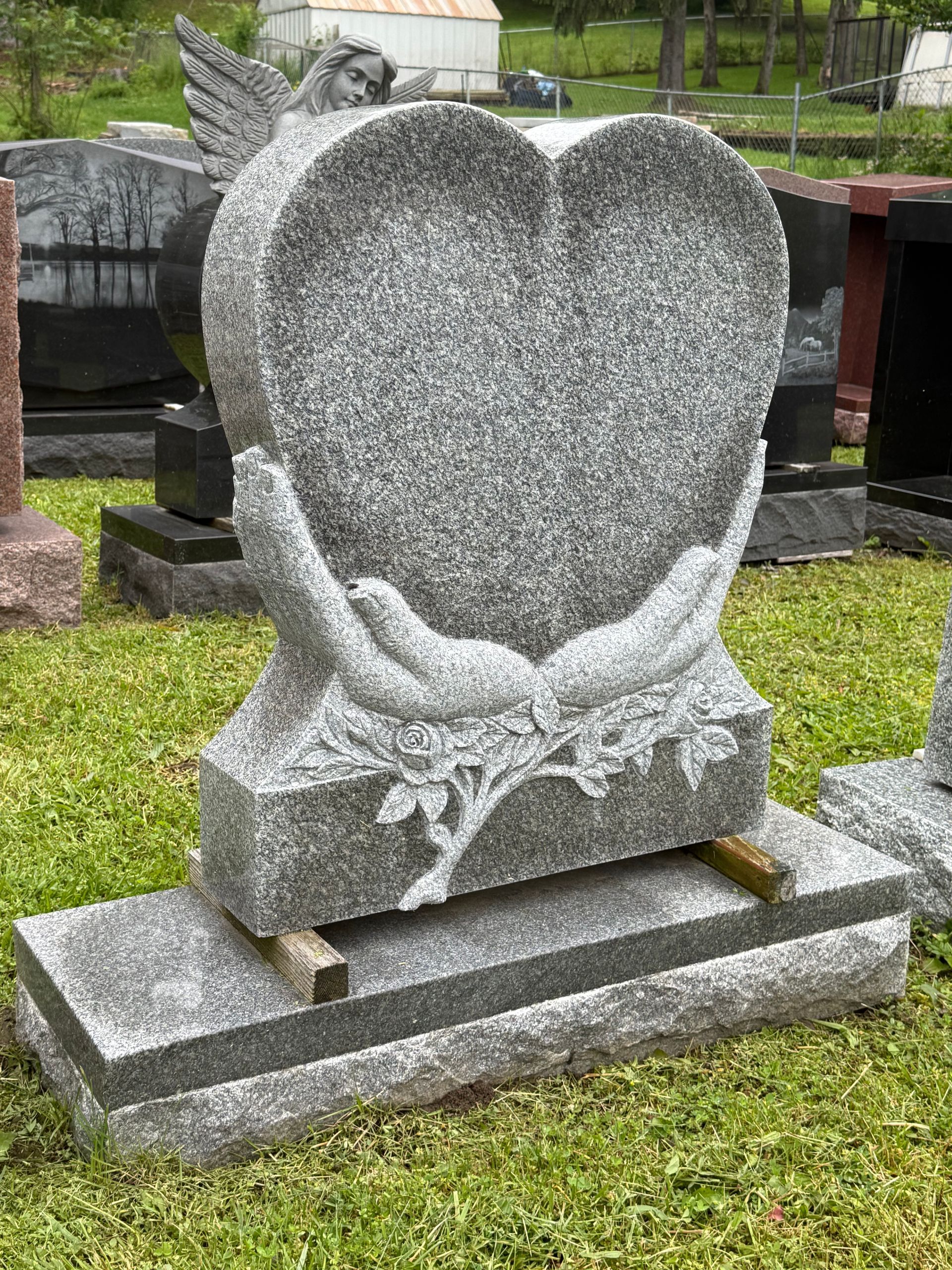 A gravestone in the shape of a heart with two hands holding it.