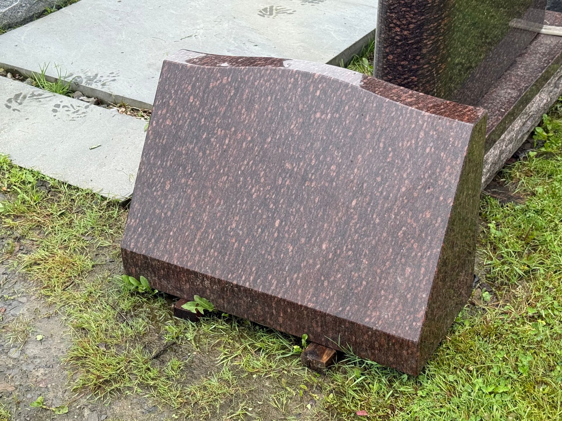 A gravestone is laying on the ground in a cemetery.