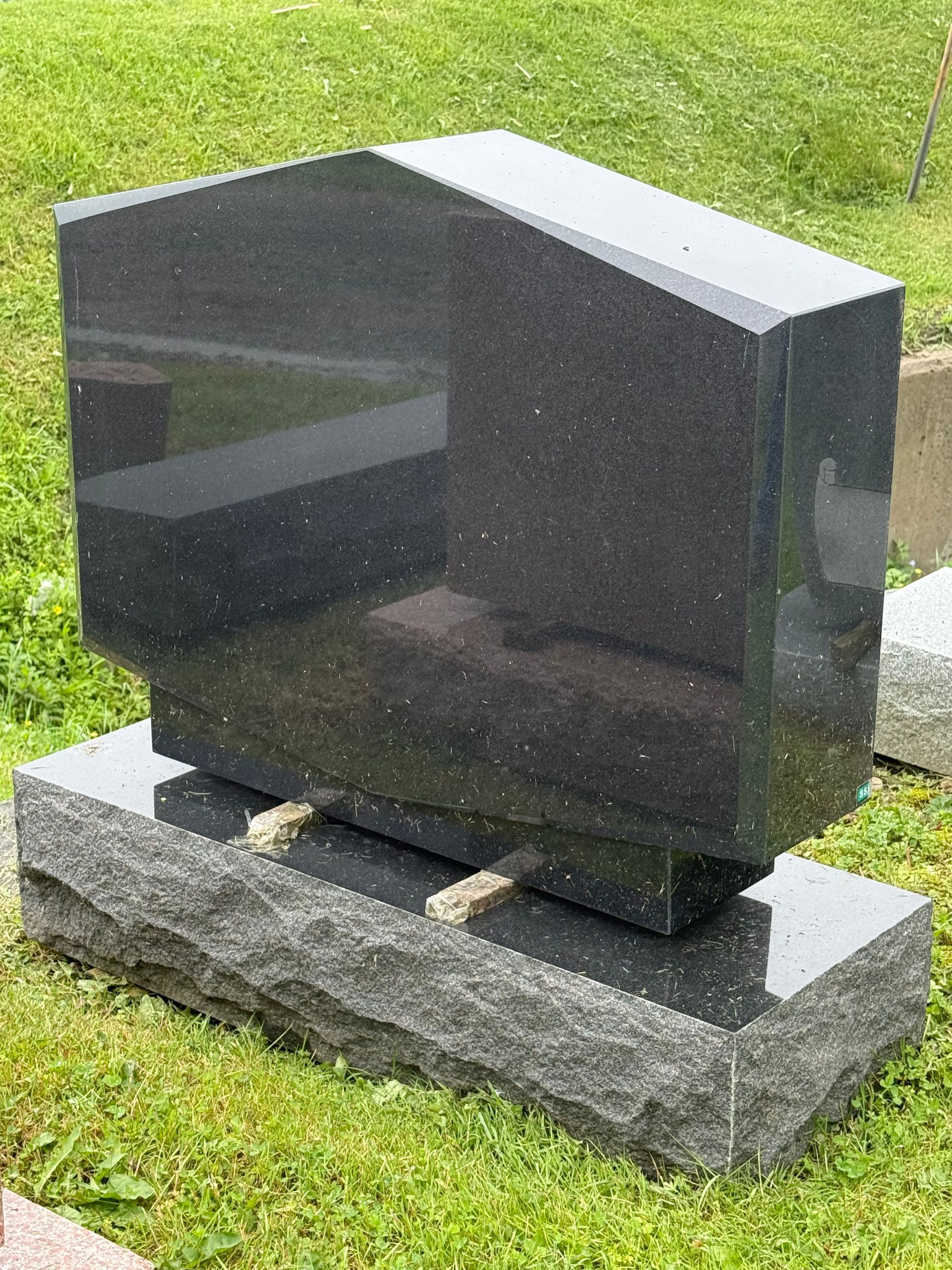 A black gravestone is sitting in the grass in a cemetery.