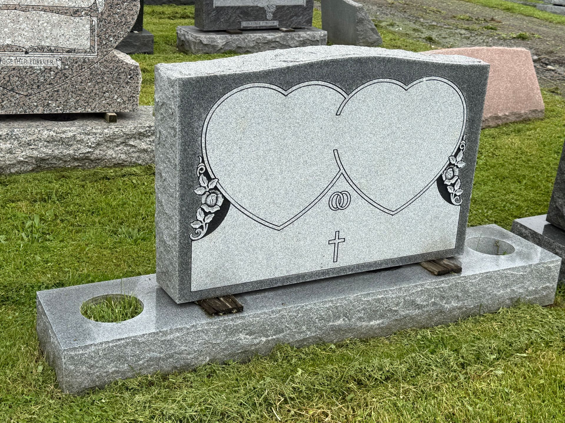 A gravestone with two hearts on it is in a cemetery.