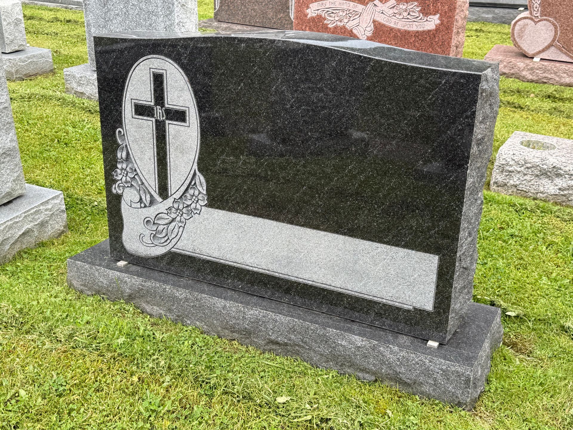 A black and white gravestone with a cross on it in a cemetery.