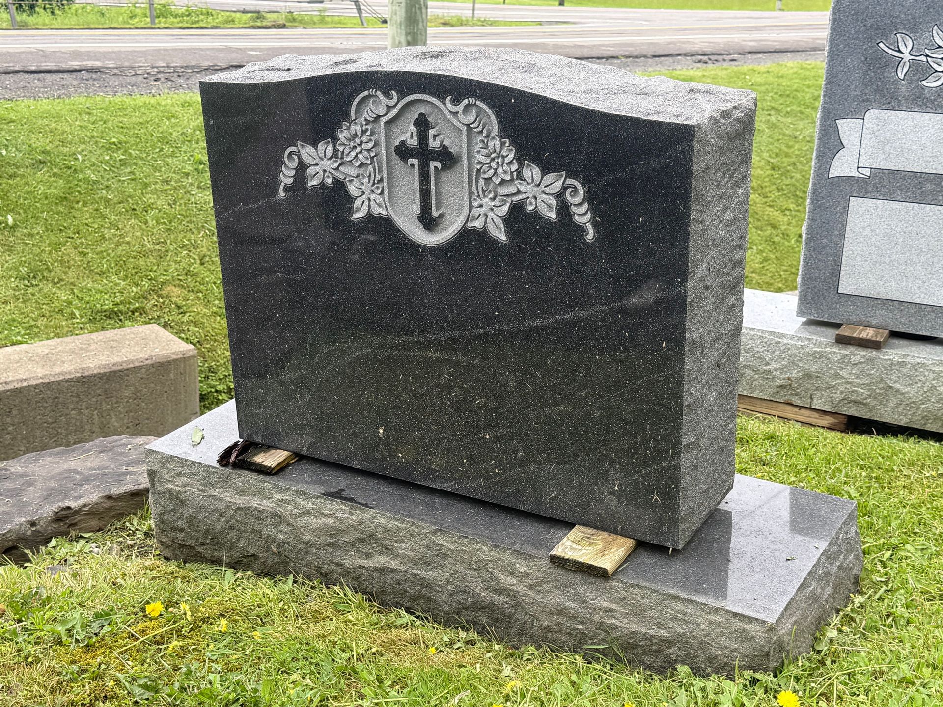 A black gravestone with a cross on it is sitting in the grass.