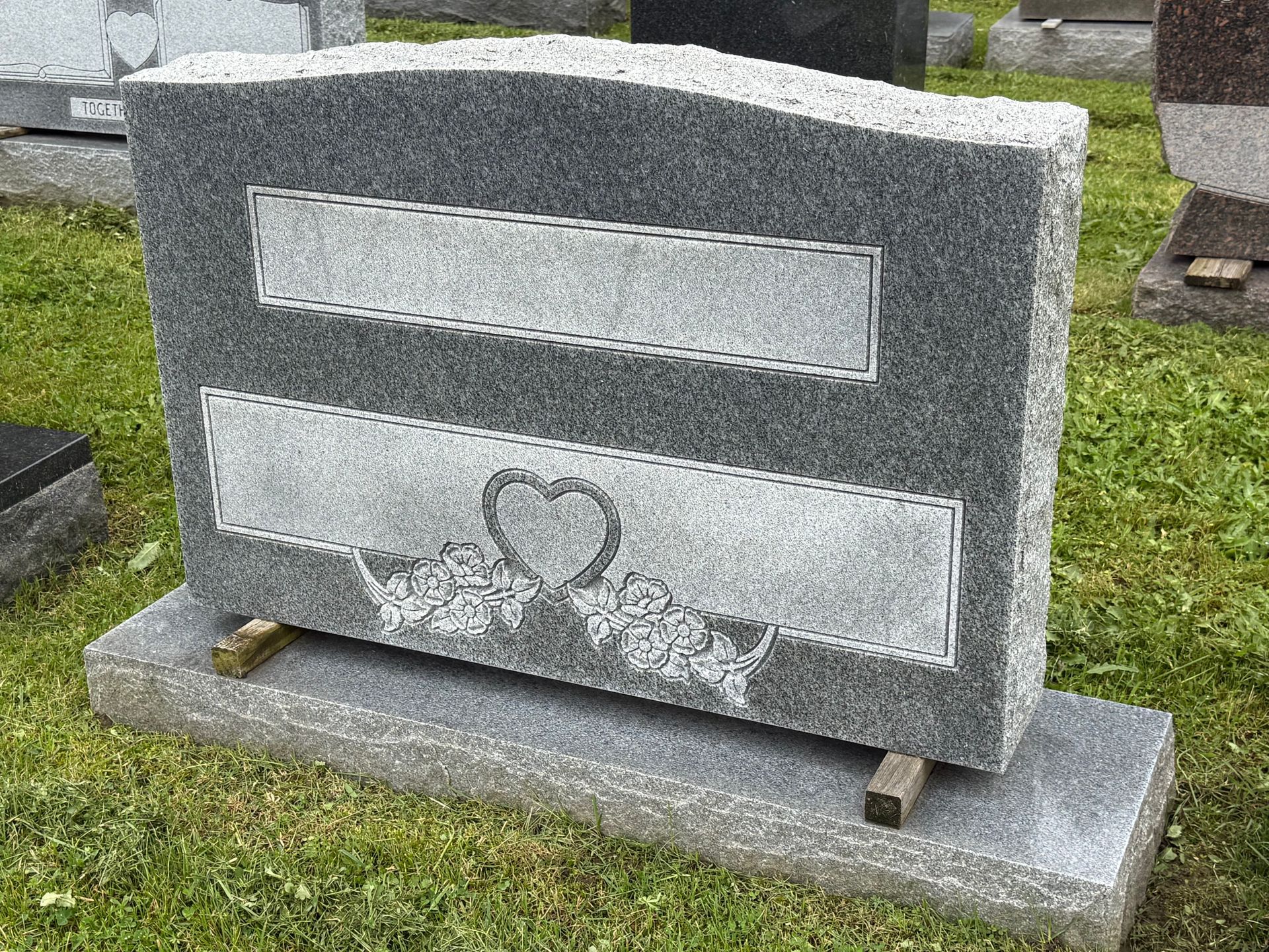 A gravestone with a heart carved into it is sitting in the grass in a cemetery.