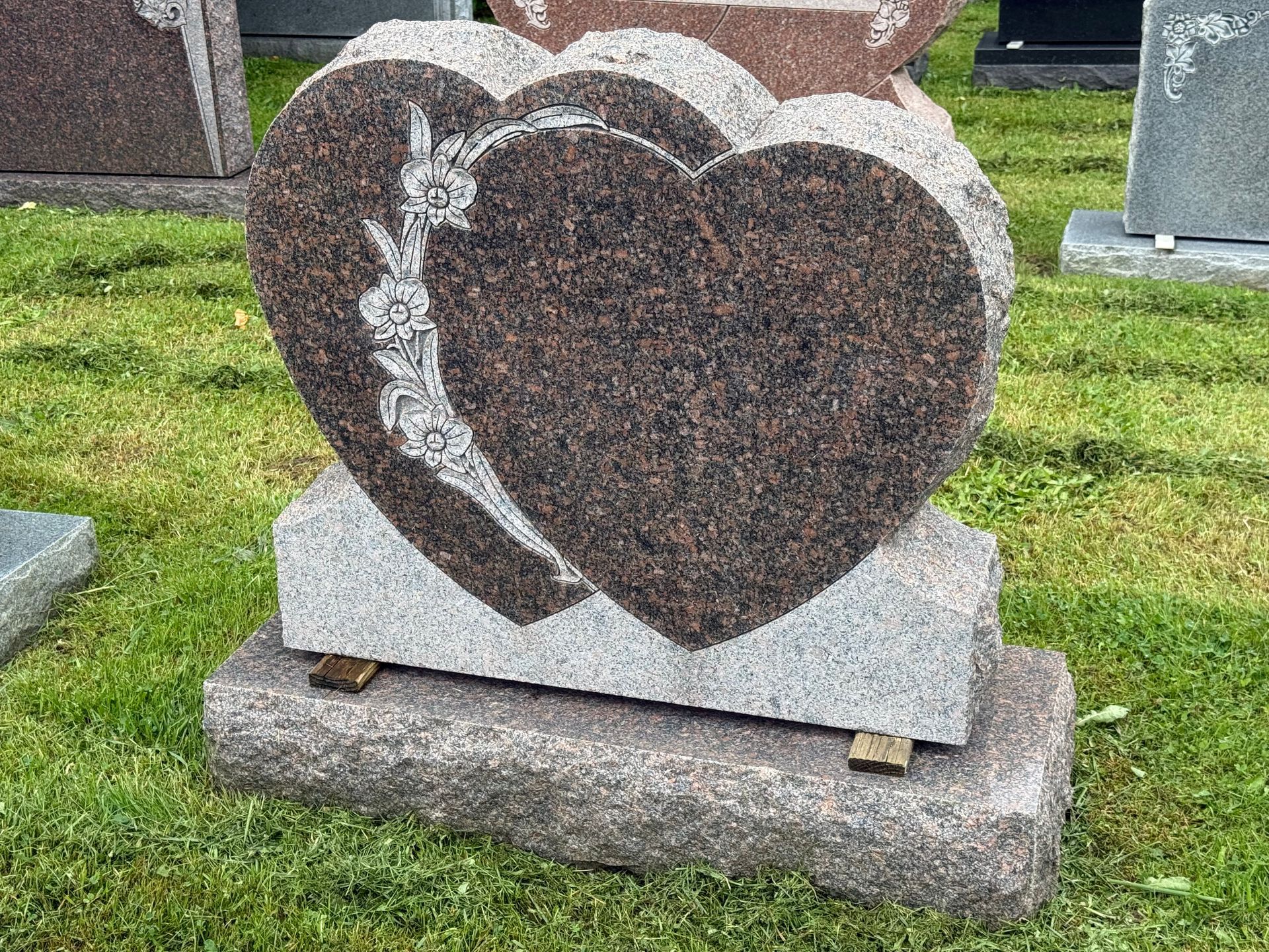 A gravestone in the shape of a heart is sitting in the grass.