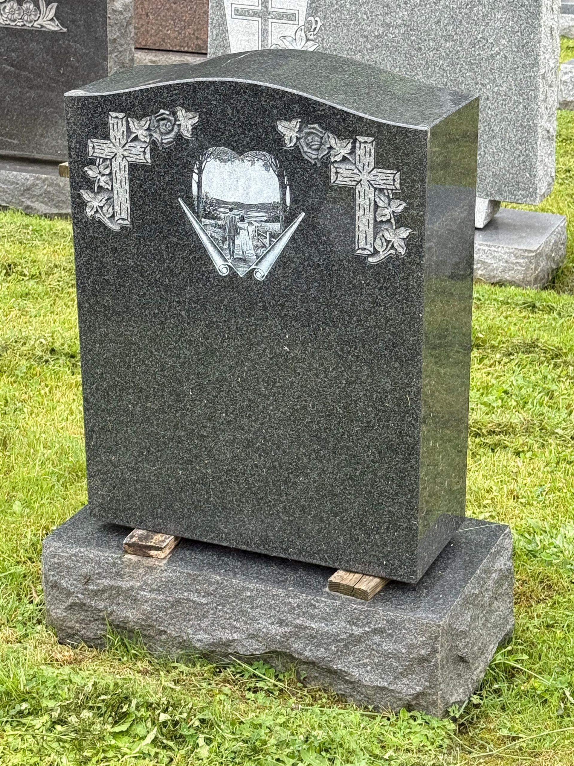 A black gravestone is sitting in the grass in a cemetery.