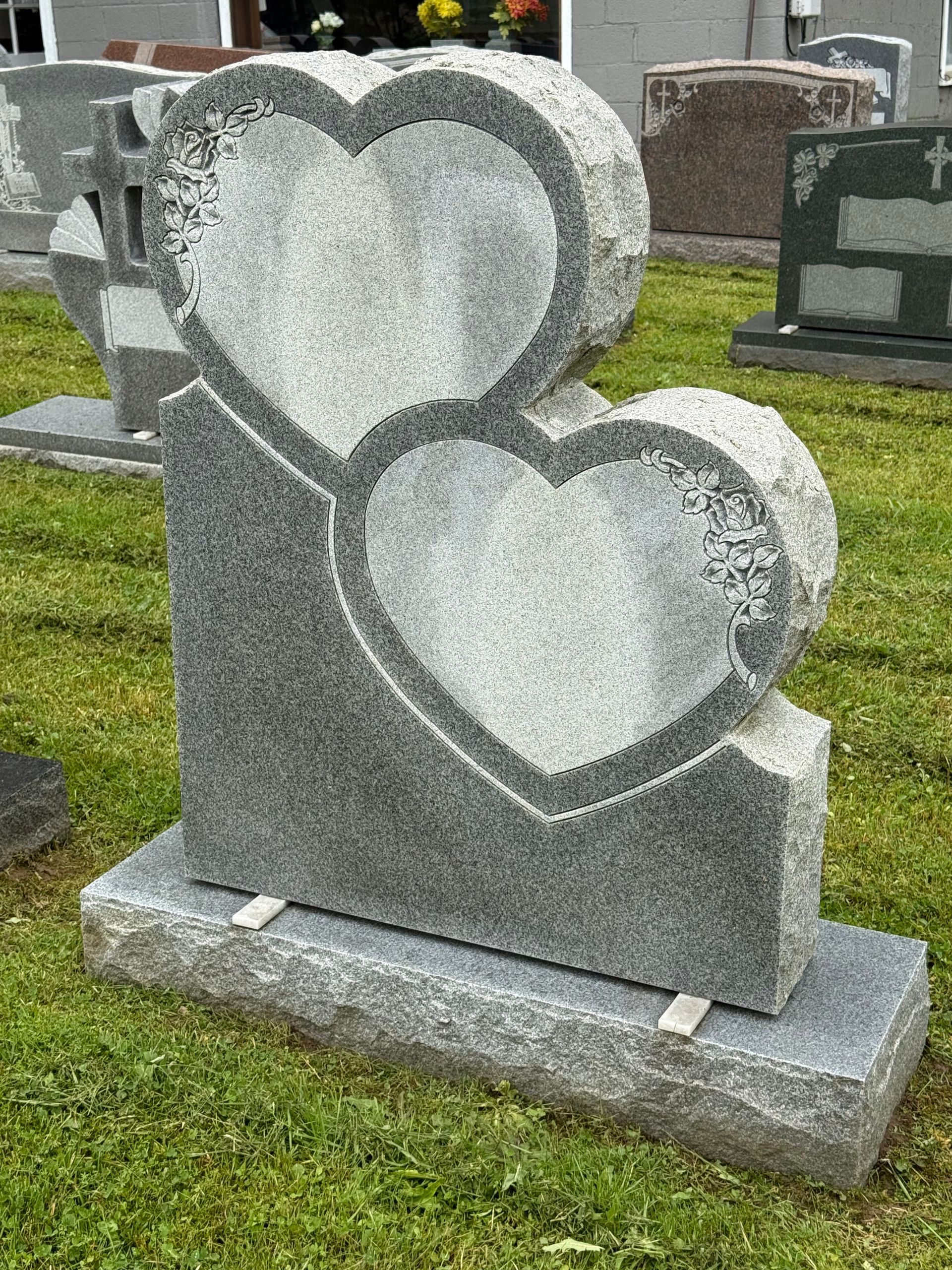 A gravestone with two hearts carved into it is in a cemetery.