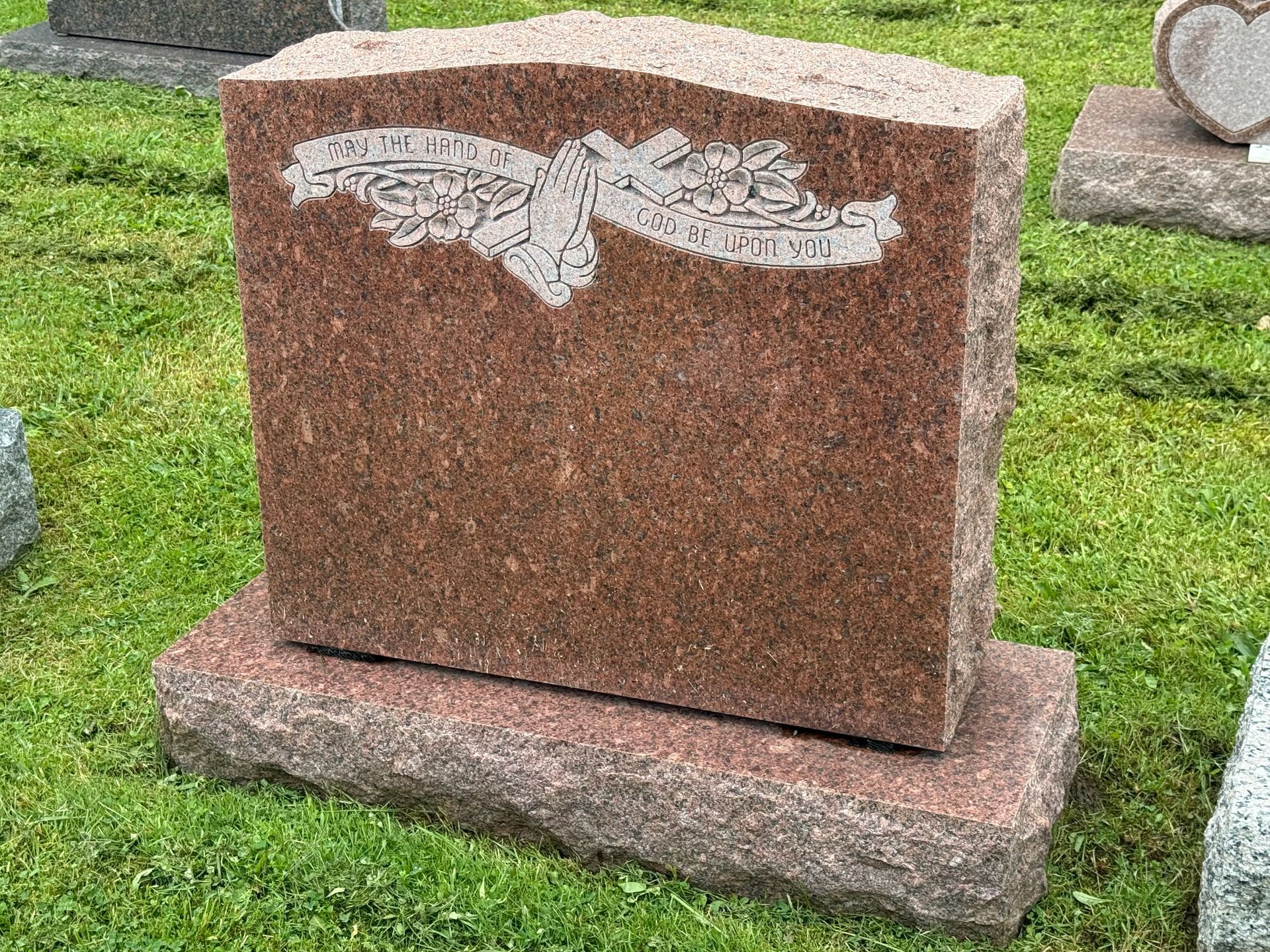 A red granite gravestone is sitting in the grass in a cemetery.
