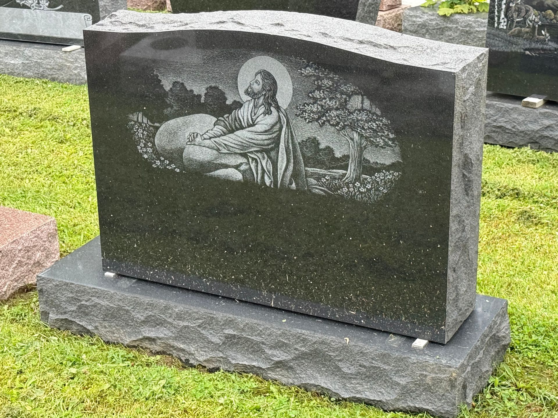 A black gravestone with a picture of jesus on it in a cemetery.
