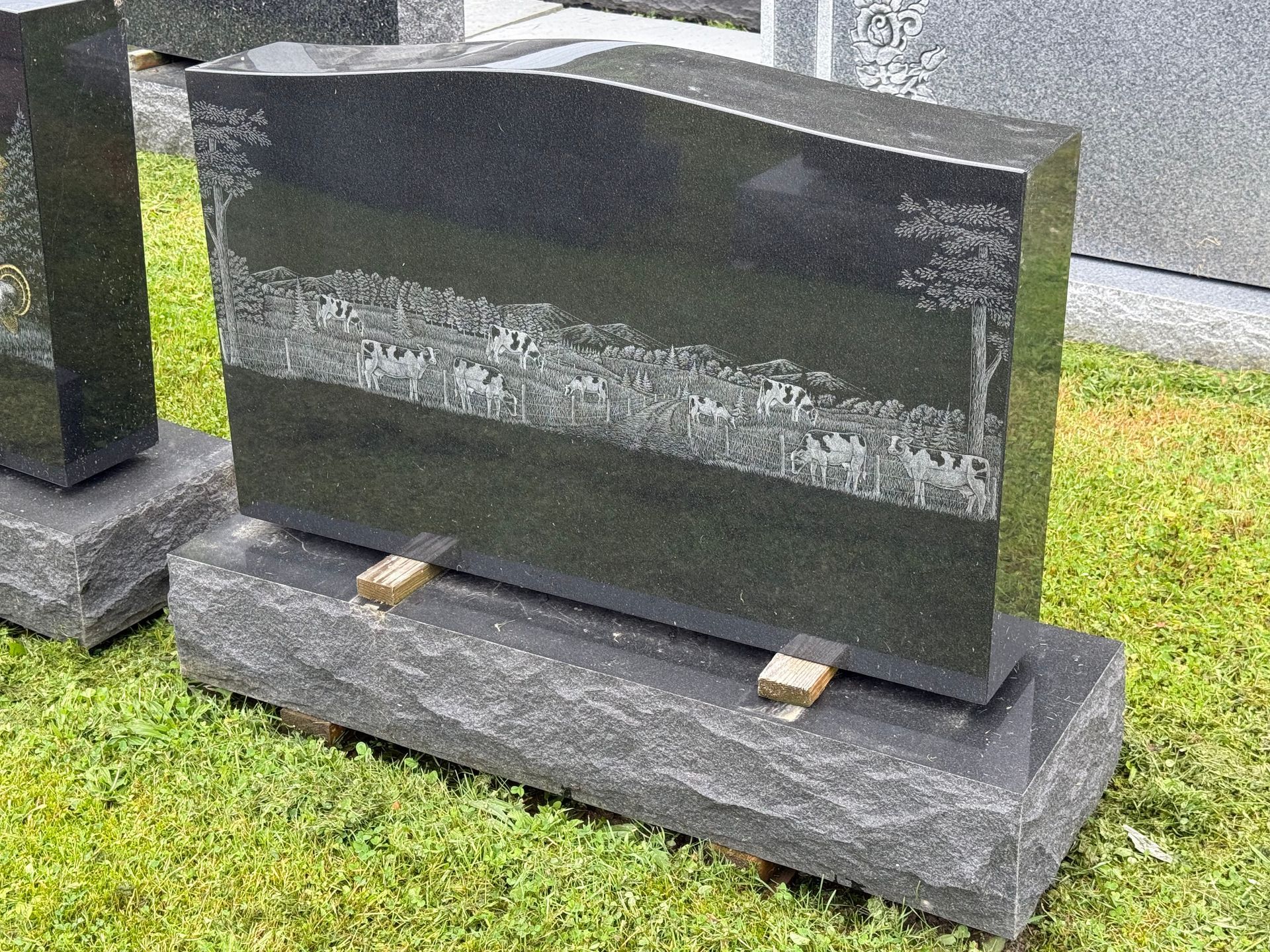 A black gravestone is sitting on top of a concrete base in a cemetery.