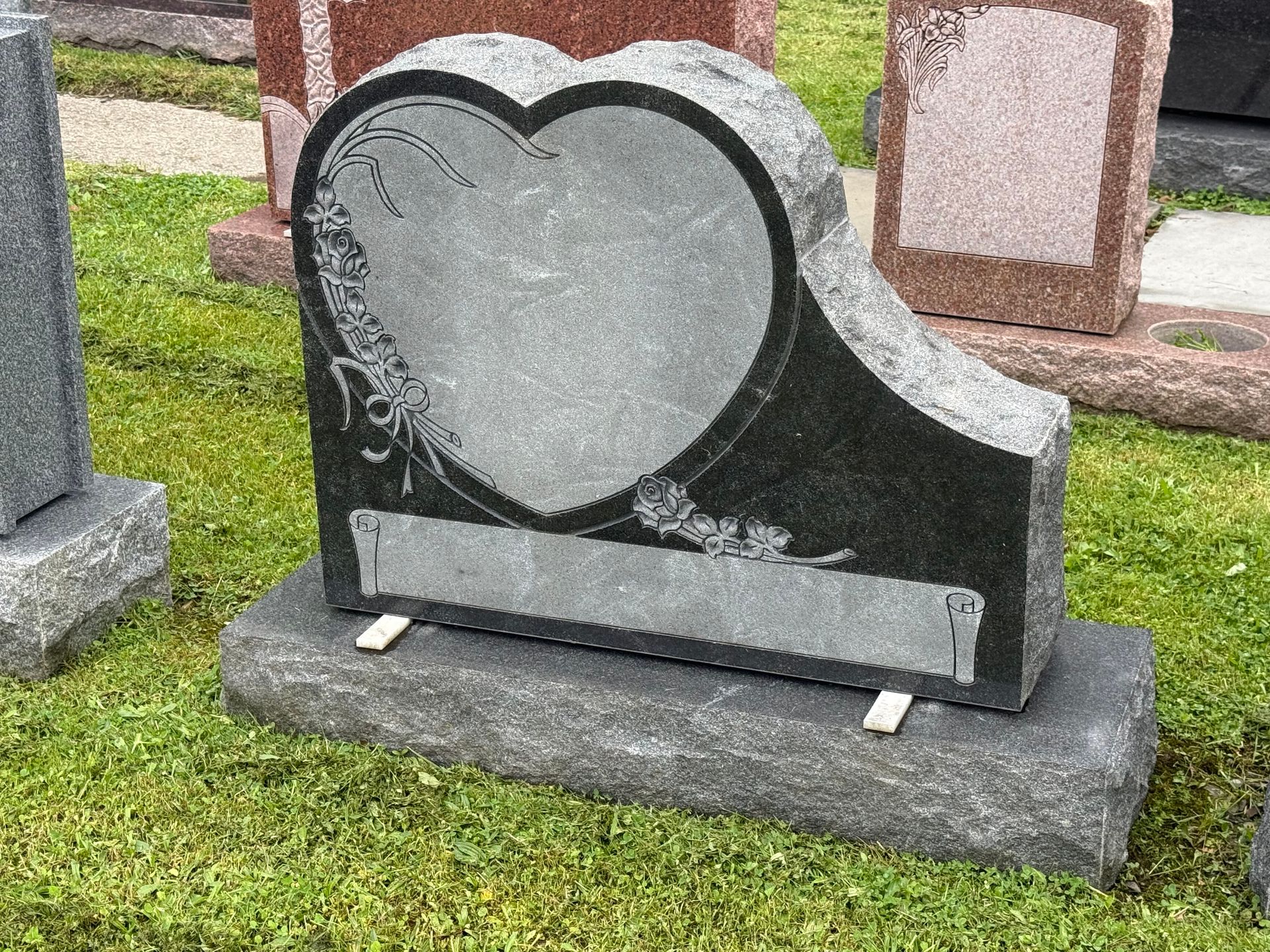 A gravestone in the shape of a heart is sitting in the grass.