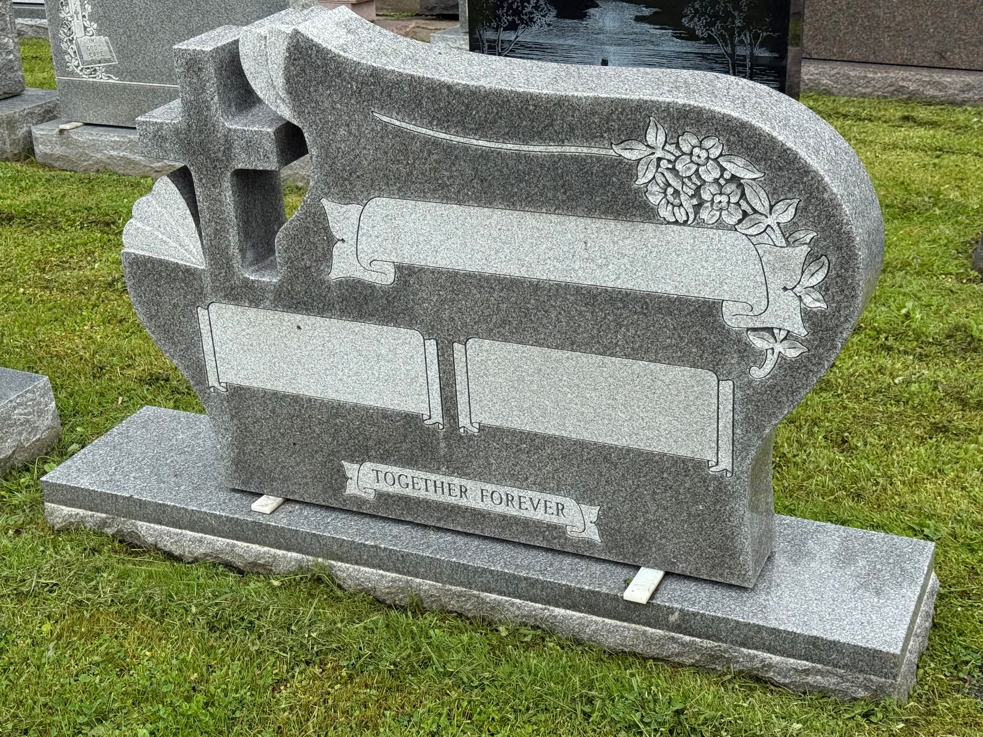 A gravestone with a cross on it is sitting on top of a lush green field.