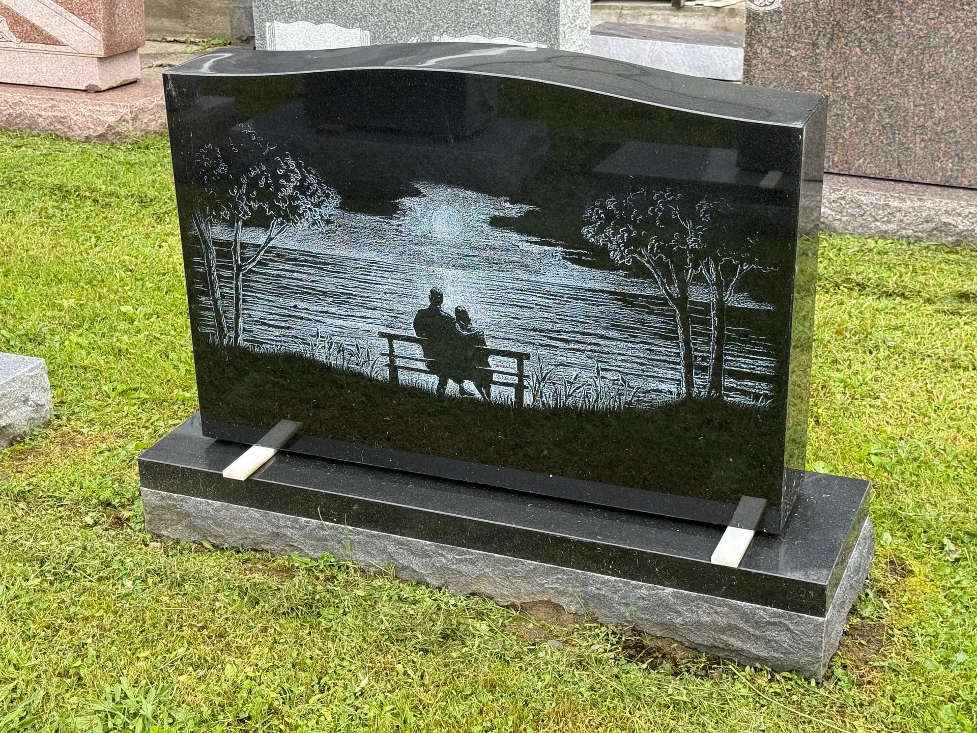 A black gravestone with a picture of a couple sitting on a bench near a lake.