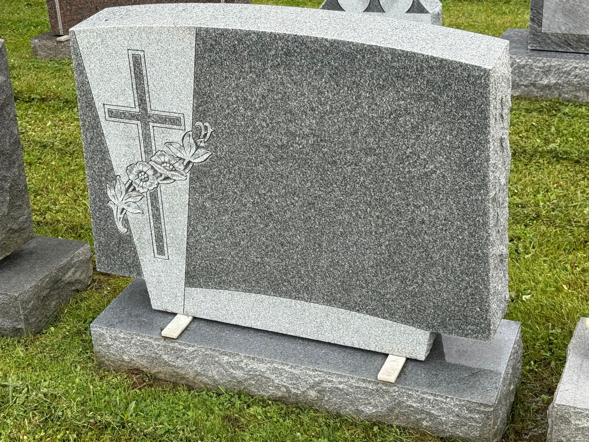 A gravestone with a cross on it is sitting in the grass.