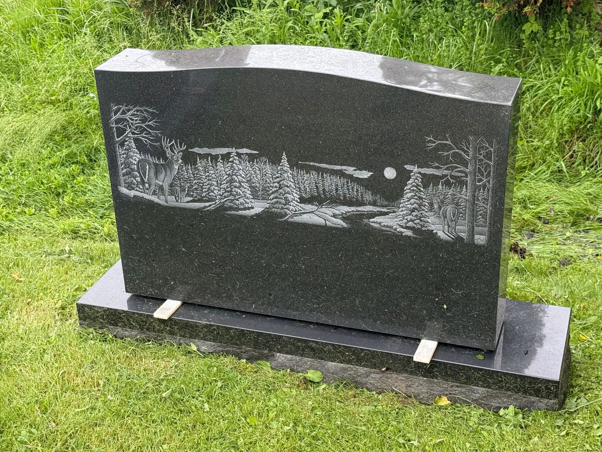 A black gravestone is sitting in the grass in a cemetery.