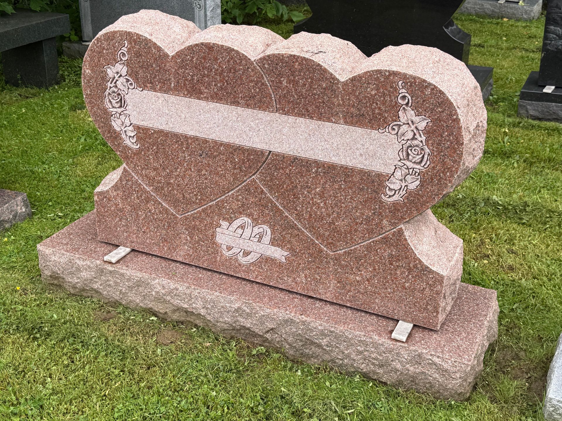 A gravestone in the shape of a heart is sitting in the grass.