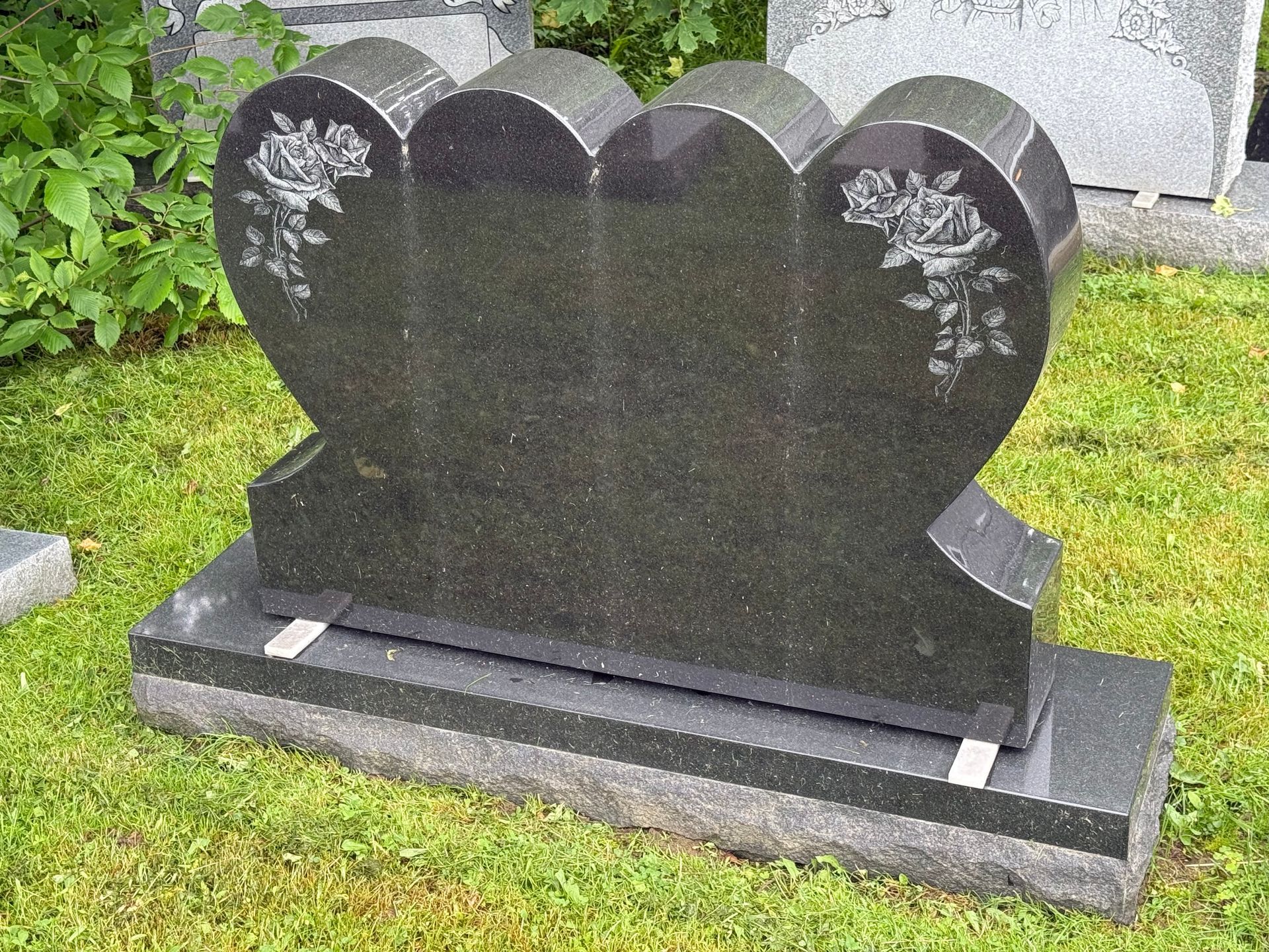 A black heart shaped gravestone is sitting in the grass.