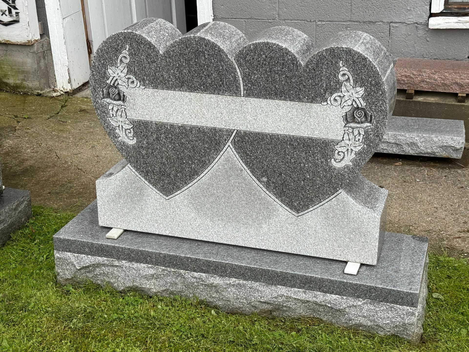 A gravestone in the shape of two hearts is sitting on top of a lush green field.