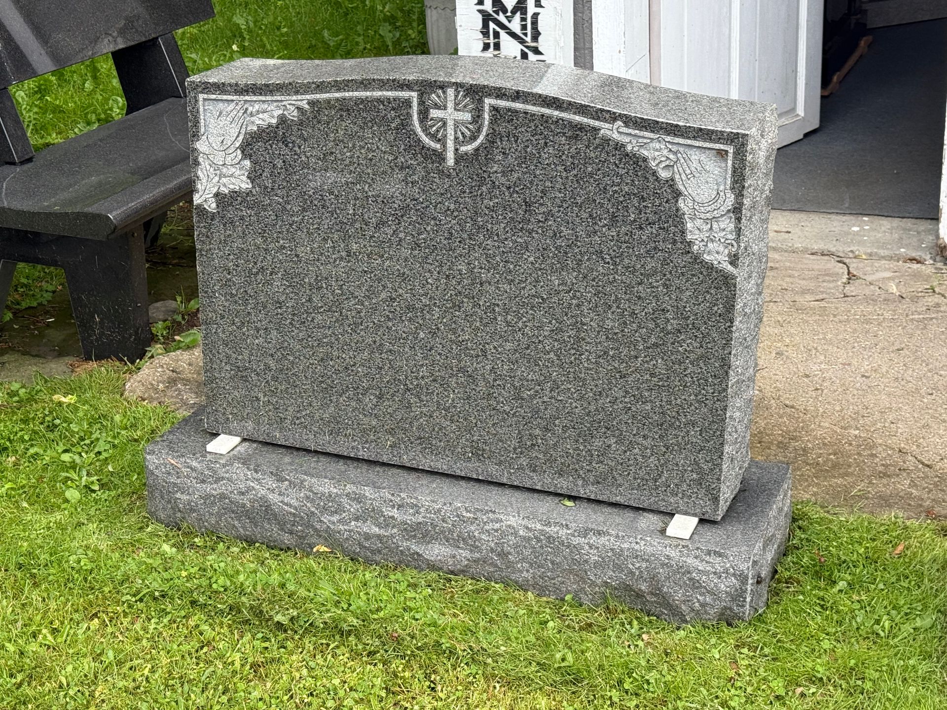 A gravestone is sitting in the grass next to a bench.