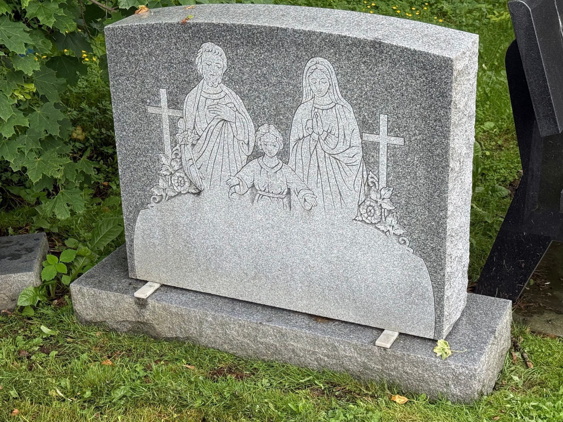 A gravestone with a picture of jesus and mary on it is sitting in the grass.