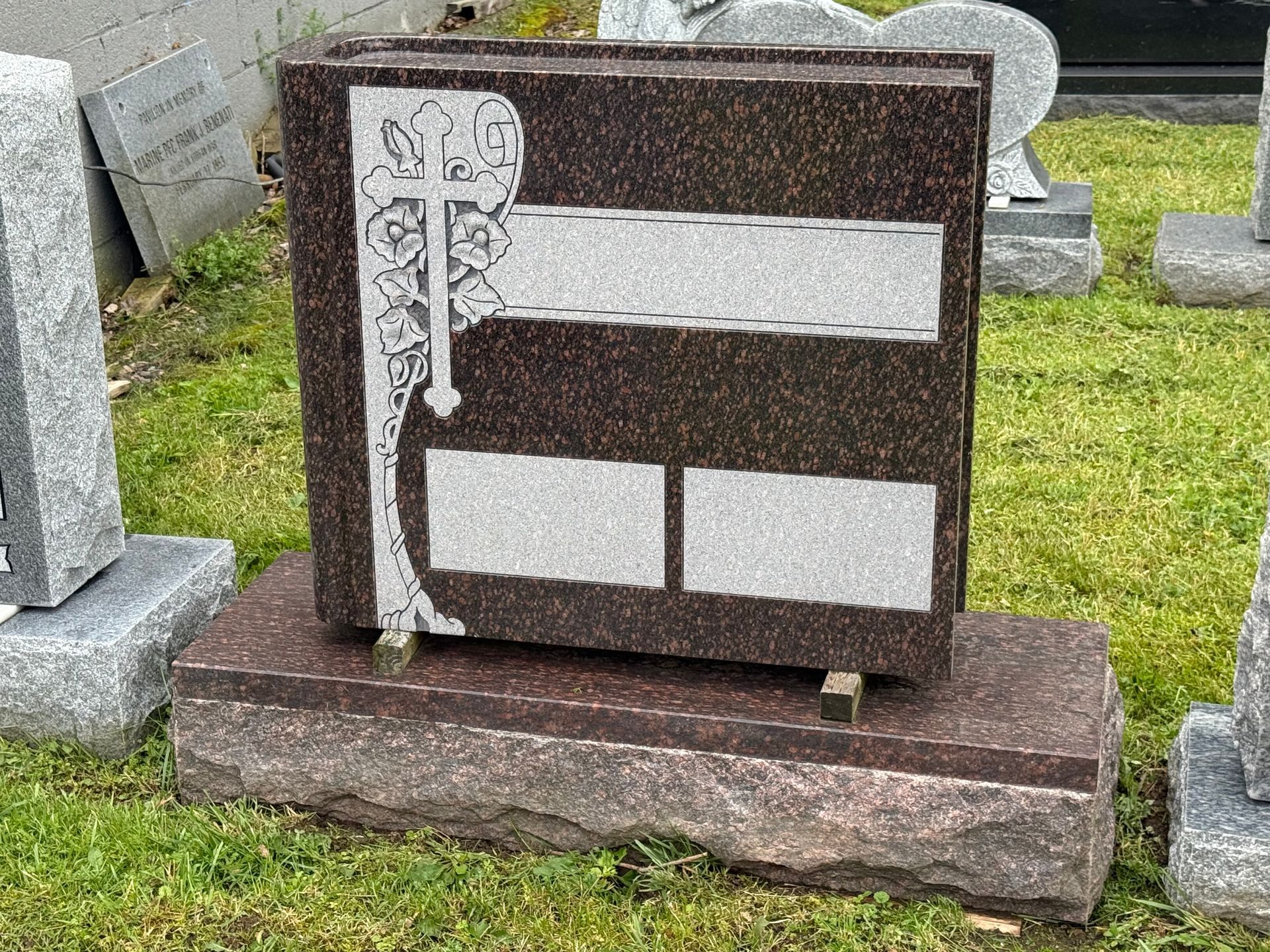 A gravestone with a cross on it is sitting in the grass in a cemetery.
