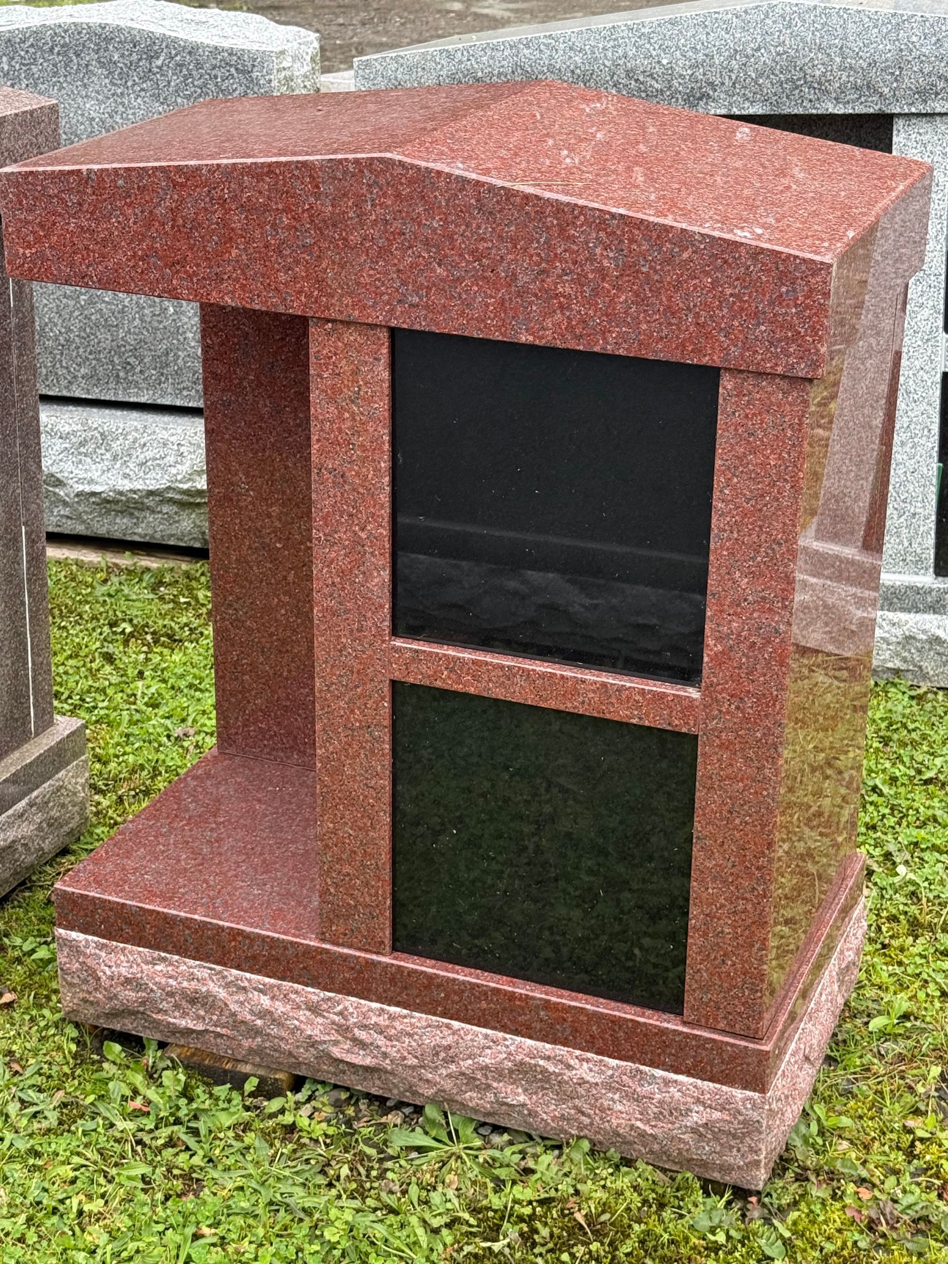 A red granite urn is sitting on top of a lush green field.
