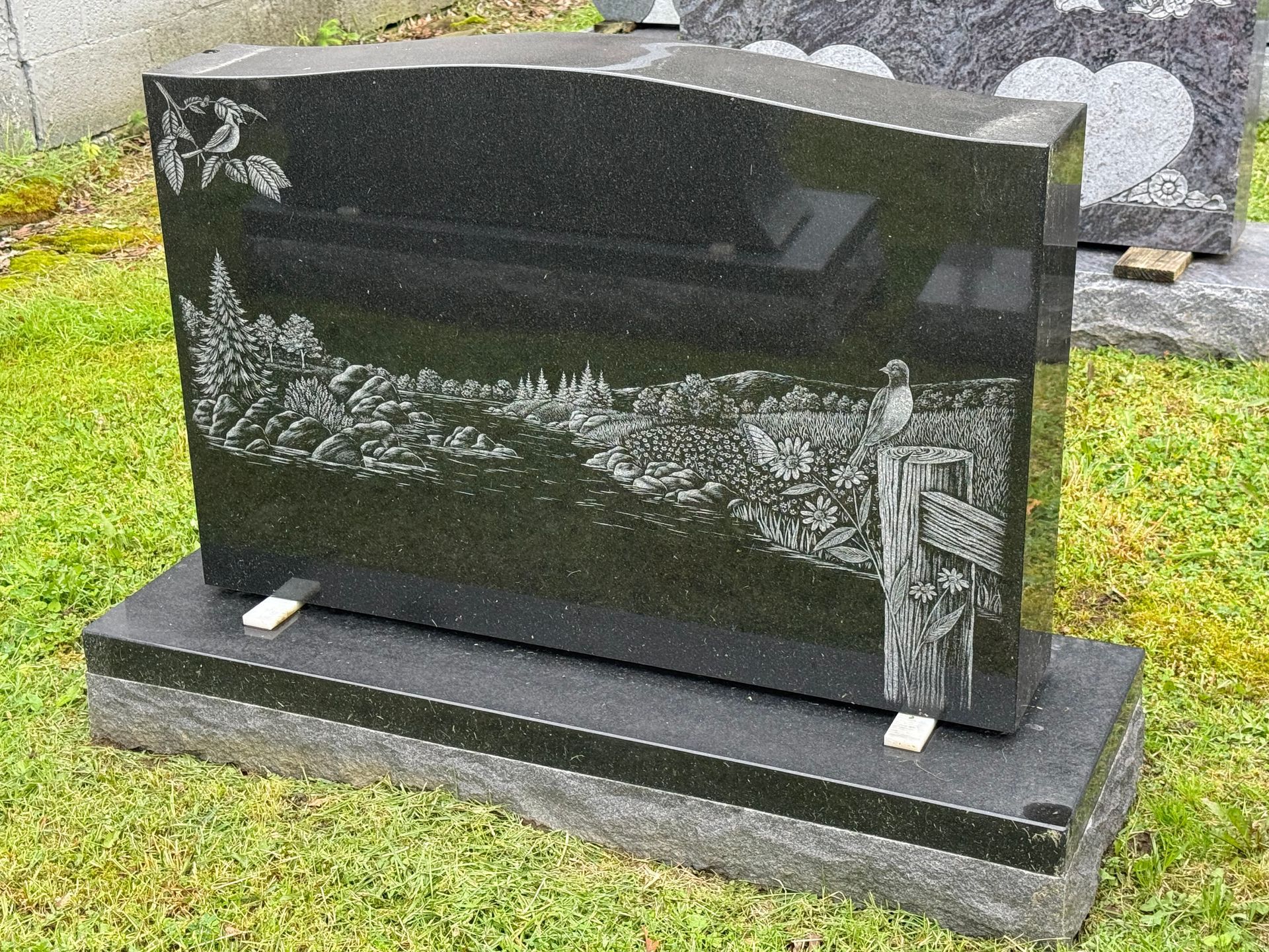 A black gravestone with a picture of a tree on it is in a cemetery.