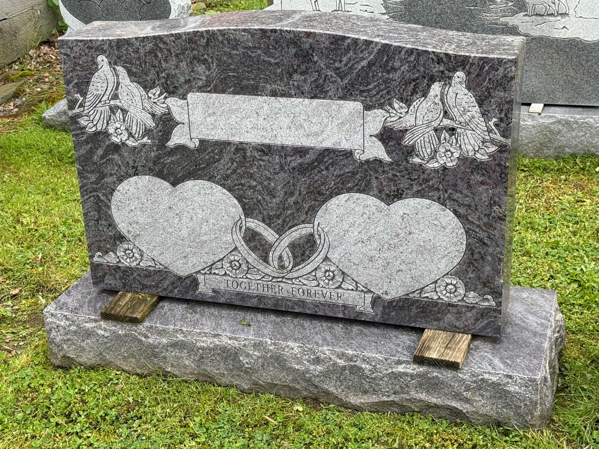 A gravestone with two hearts carved into it is in a cemetery.