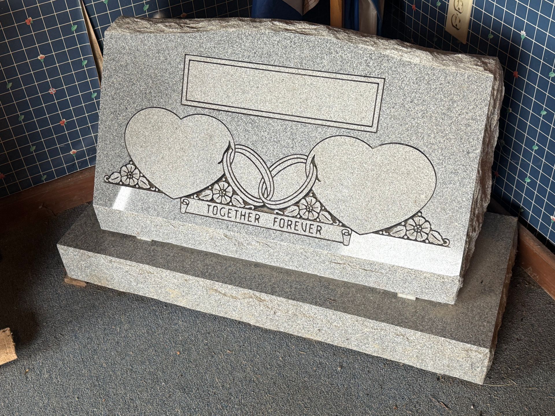 A gravestone with two hearts on it is sitting on a carpet.
