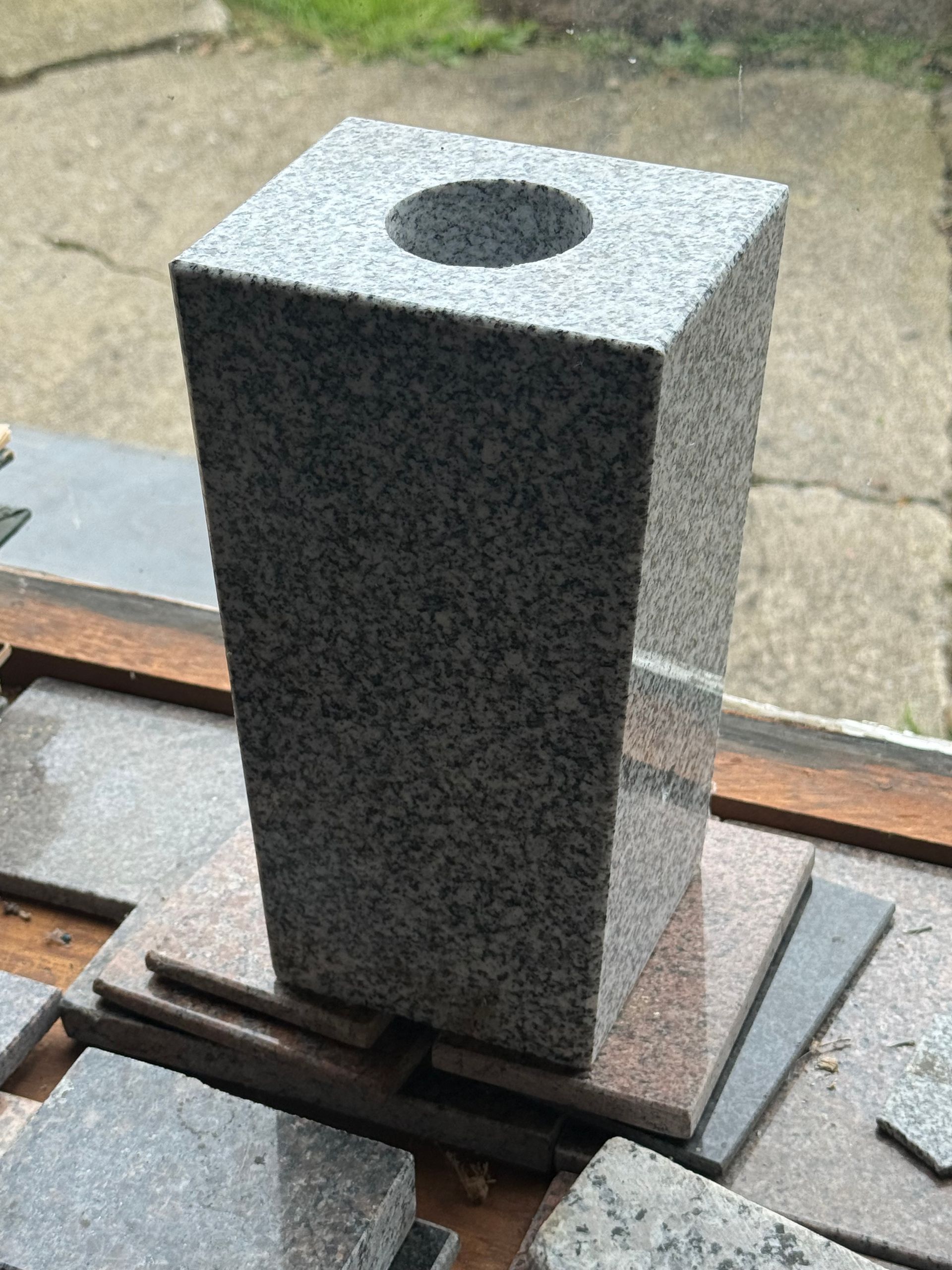 A square stone vase with a hole in the middle is sitting on a table.
