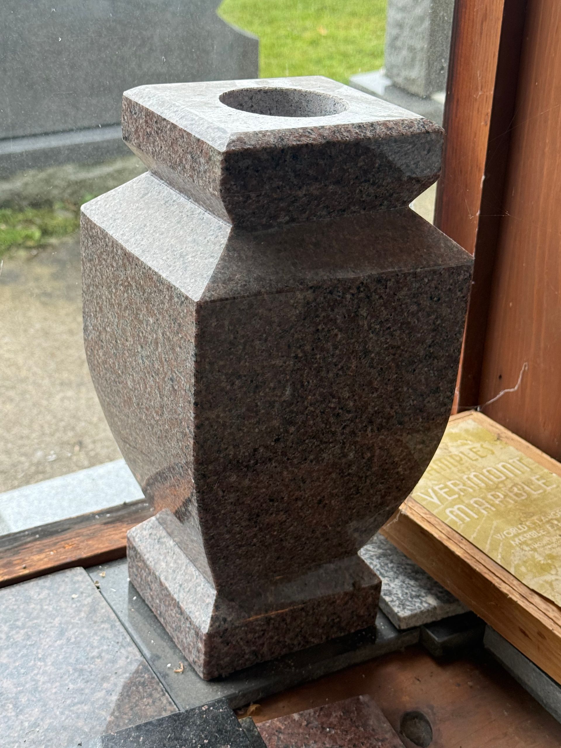 A stone vase with a hole in the middle is sitting in front of a window.
