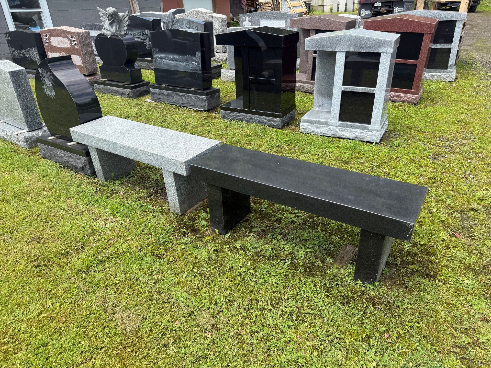 A row of gravestones and benches are sitting on top of a lush green field.