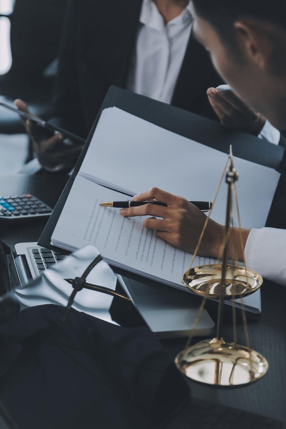 A professional reviewing a legal document at a desk with a scale of justice, a calculator, and a legal robe.