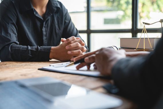 Four diverse professionals smile, gathered around a table indoors, with a tablet and coffee cup.
