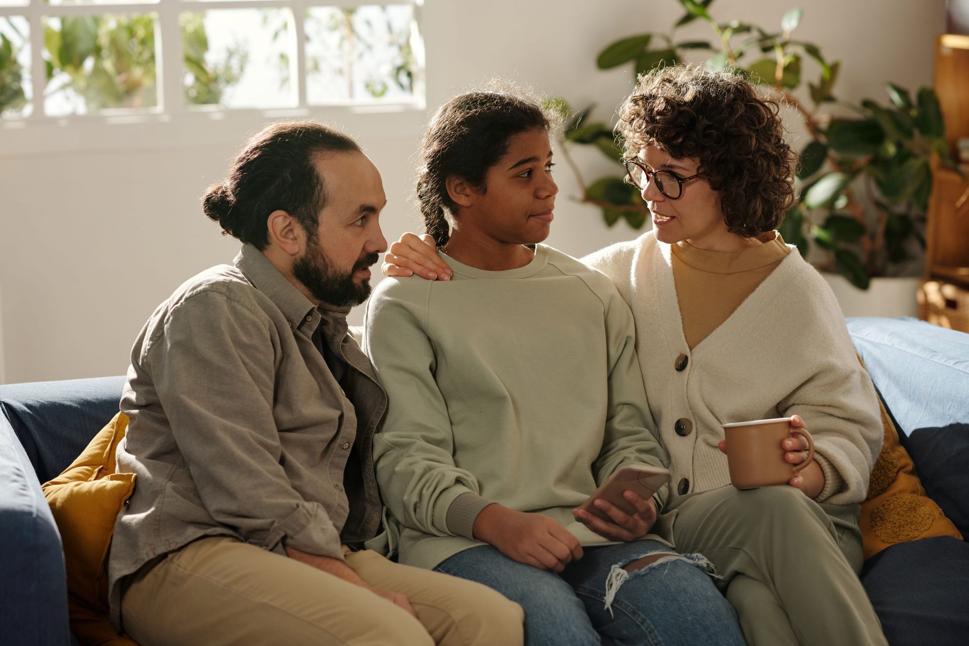 Group of diverse people laughing, gathered around a table with food and a laptop in a bright cafe.