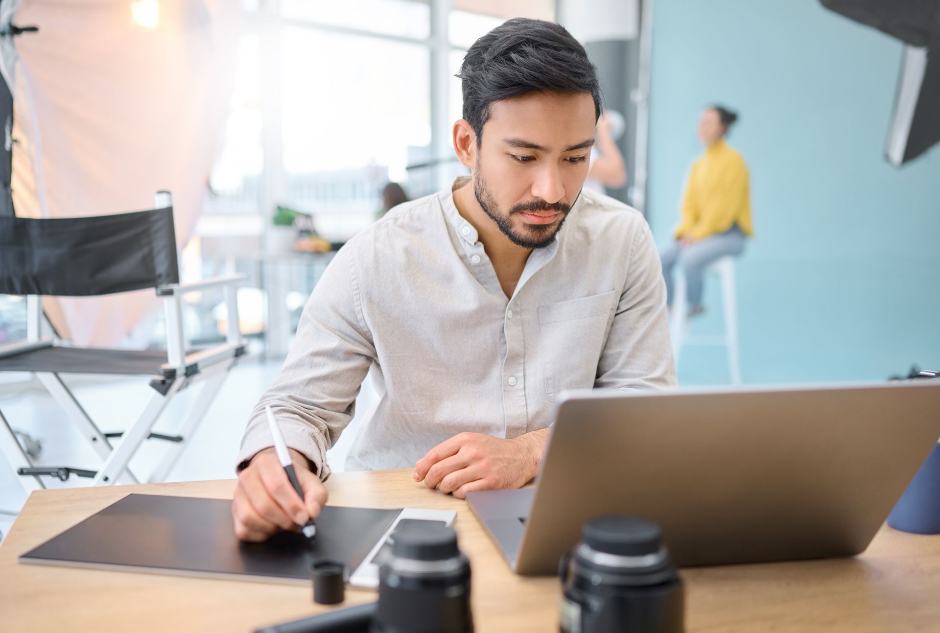 Group of diverse people laughing, gathered around a table with food and a laptop in a bright cafe.