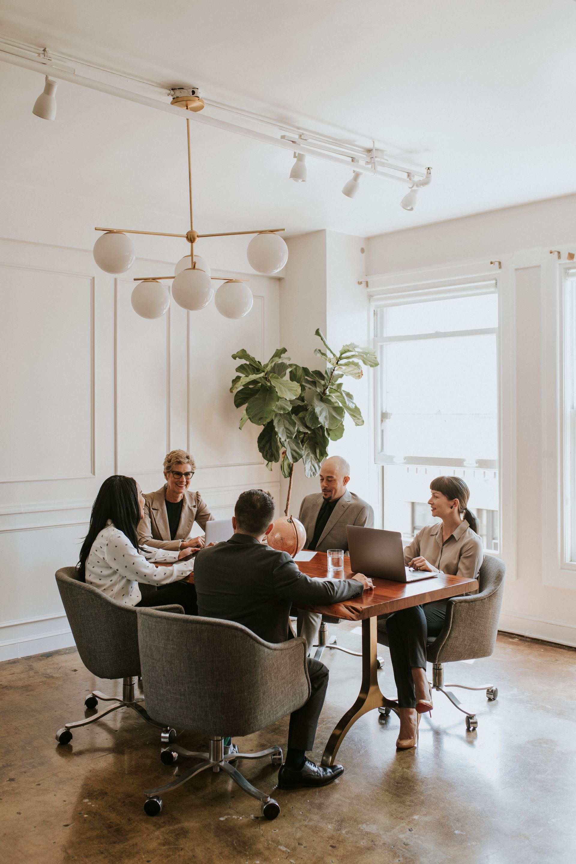 Five professionals sit around a wooden table in a bright, modern office, engaged in a collaborative meeting.