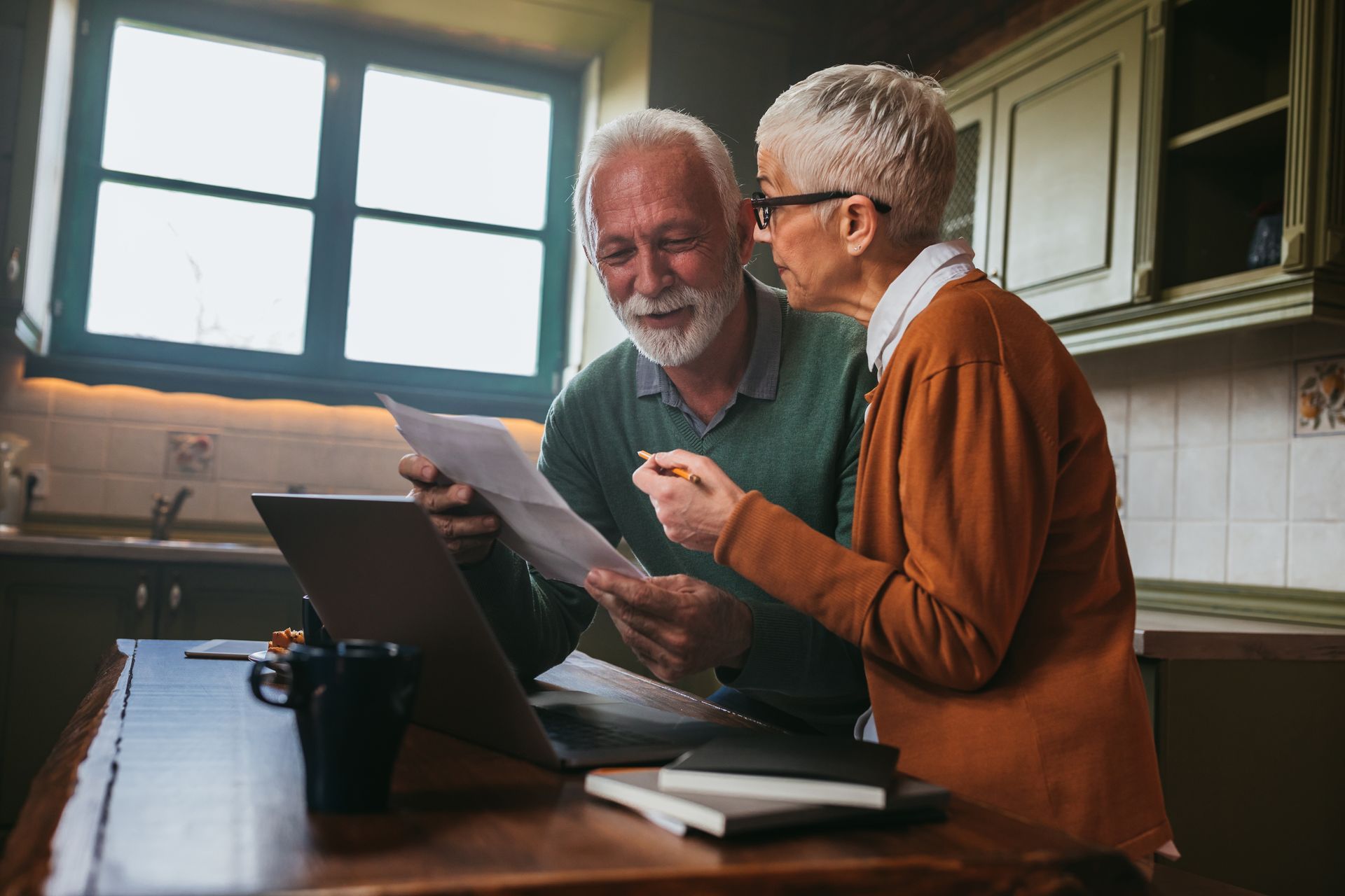 Two people reviewing documents together on a laptop in a kitchen.