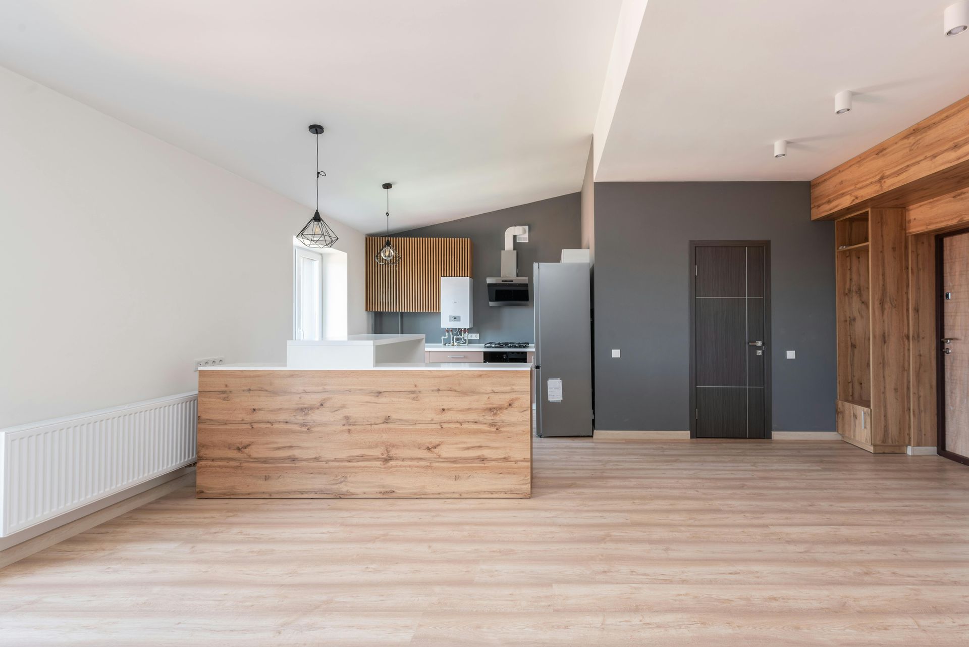 Open-concept kitchen and living area with wooden accents, gray wall, and light wood flooring.