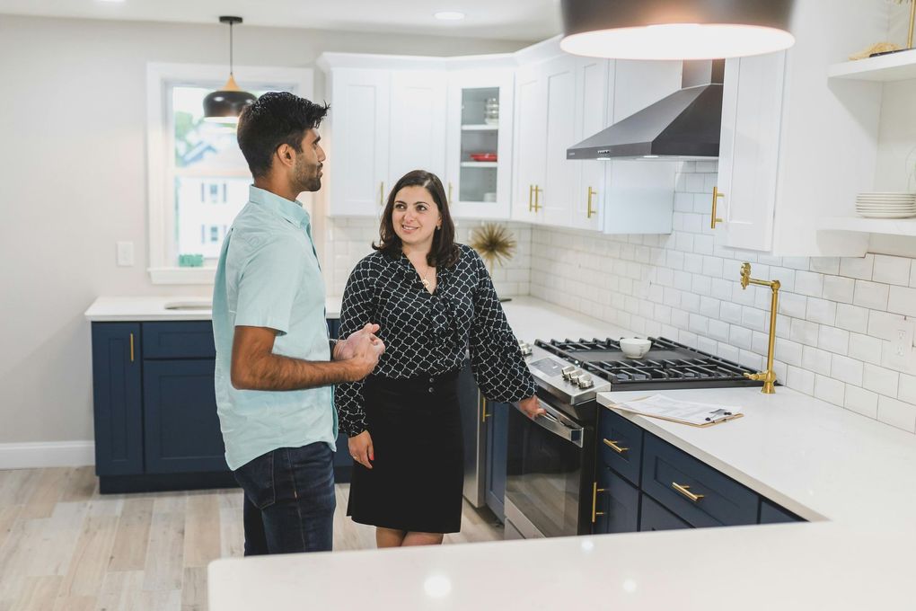 Man and woman in a modern kitchen, looking at a stove. The woman is smiling, the man is talking.